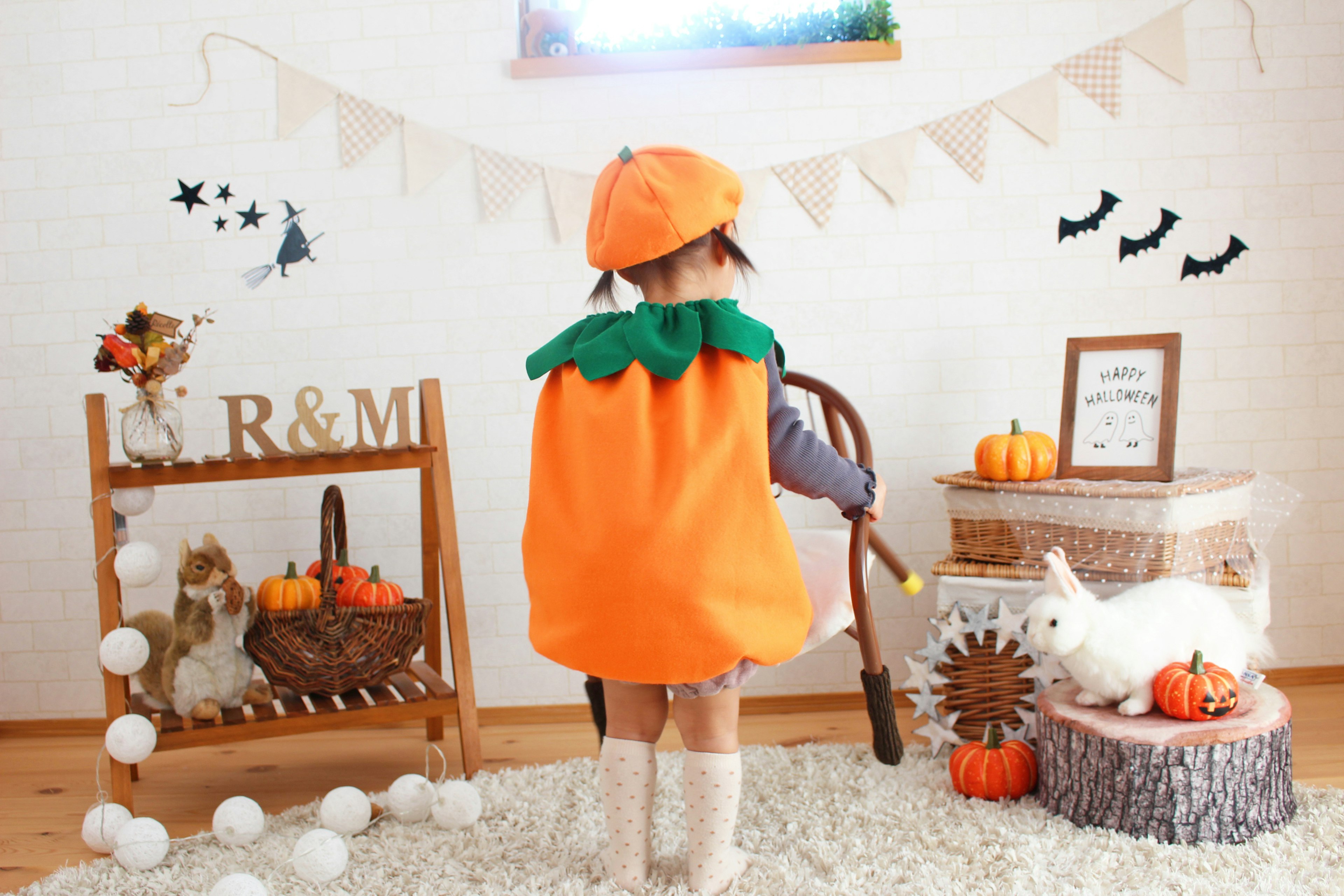 Child wearing an orange pumpkin costume standing in a cozy room with autumn decorations