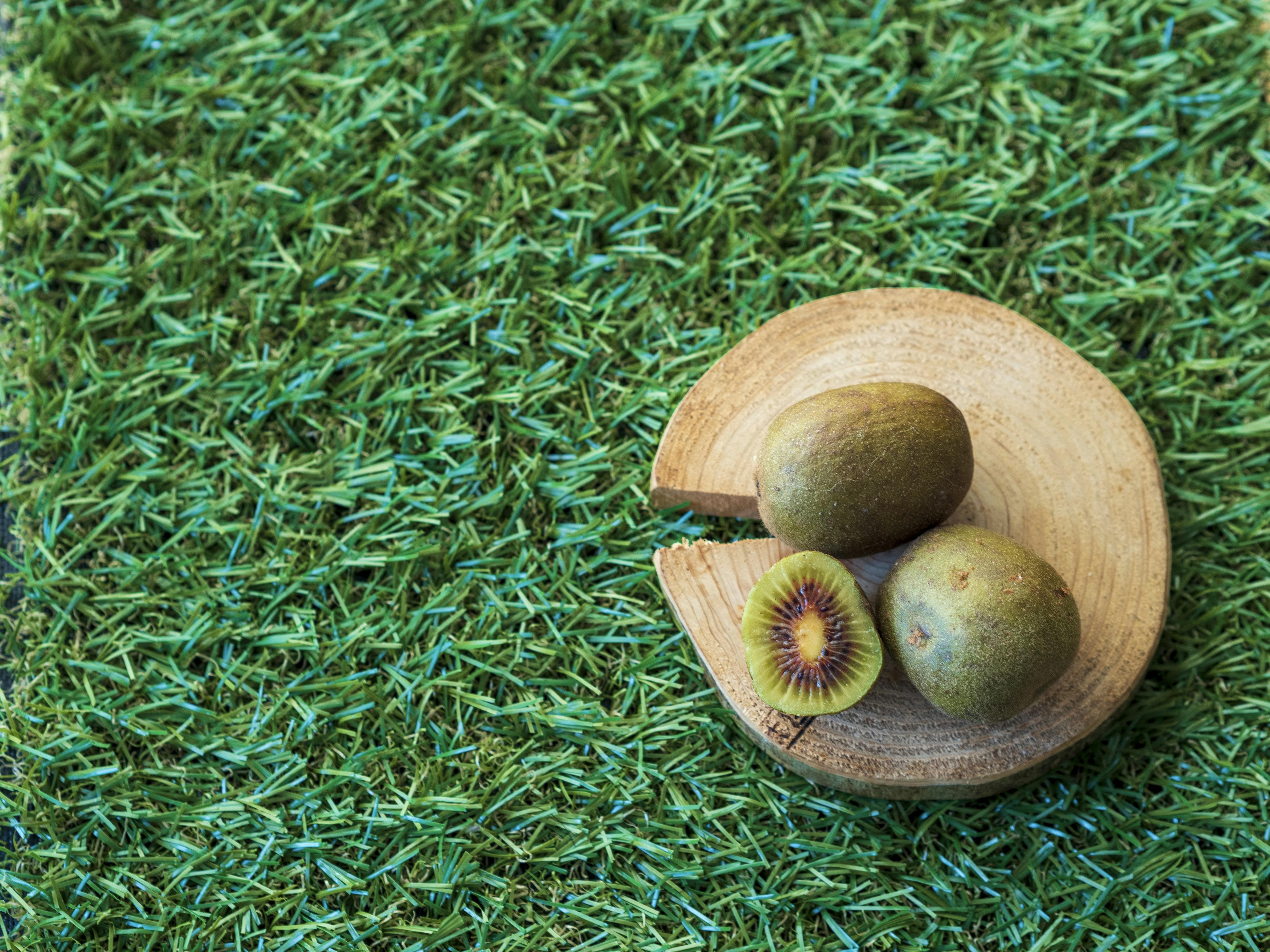 Fruits de kiwi sur une assiette en bois posée sur de l'herbe artificielle verte