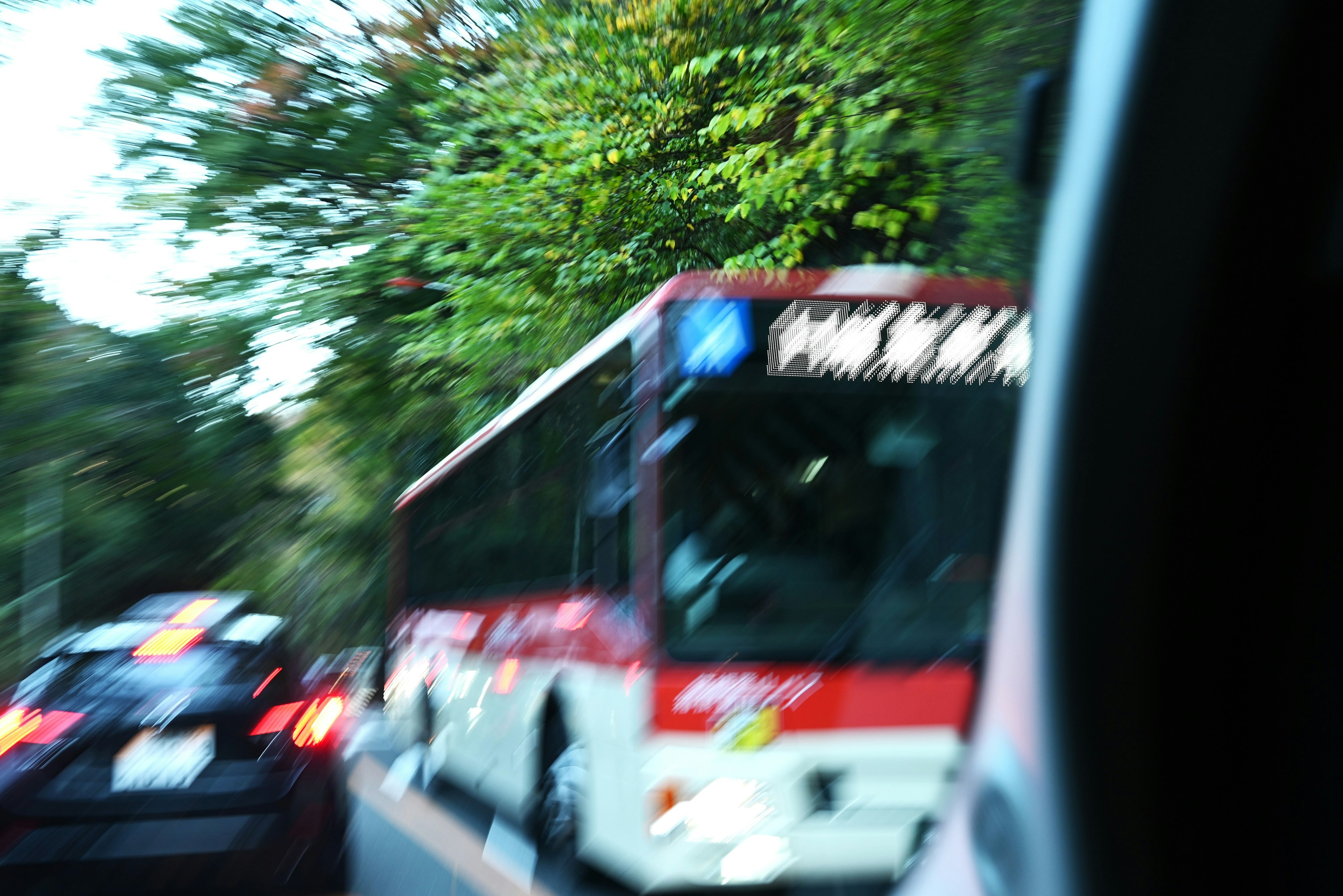 Red bus moving through blurred background with line of cars