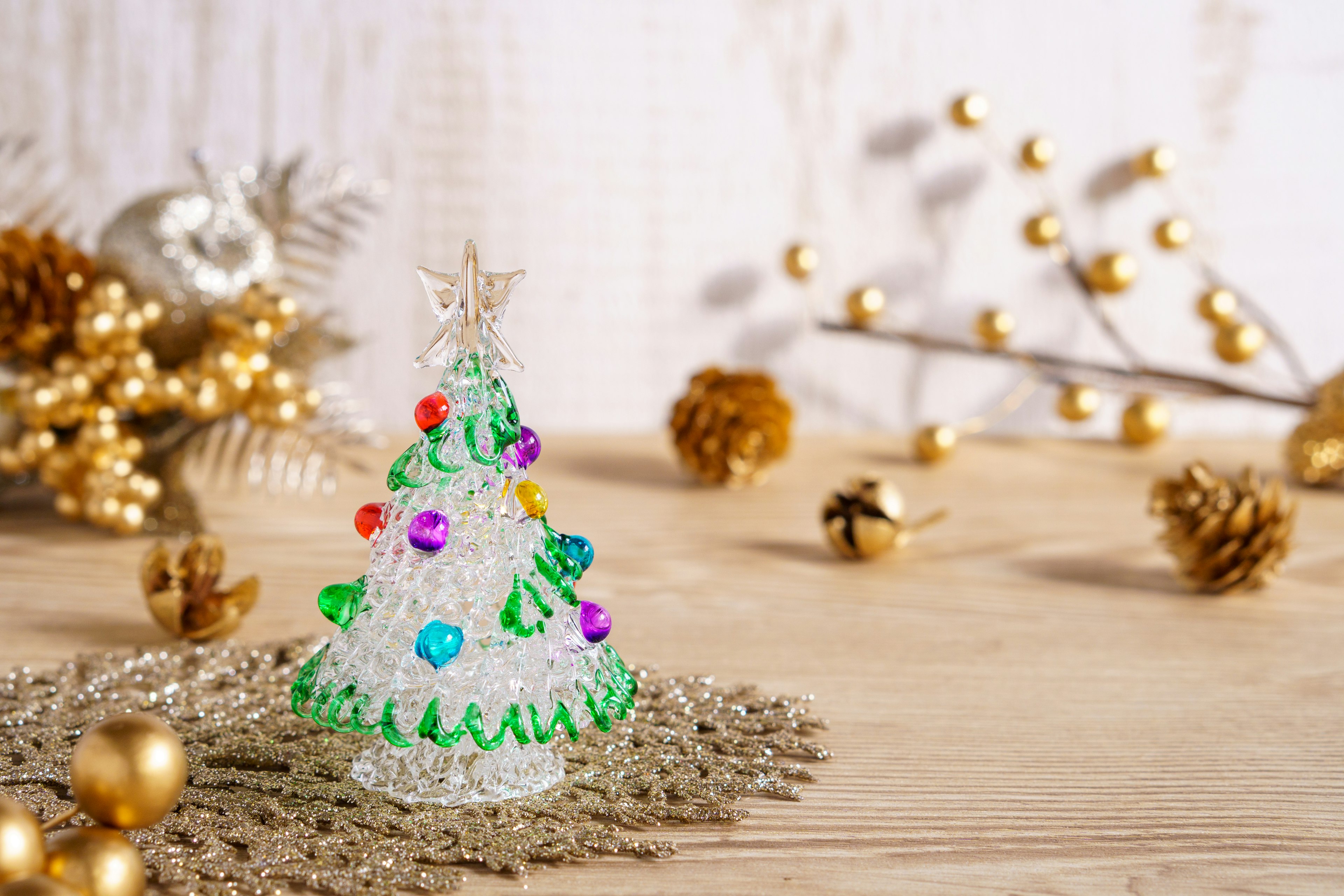 Ein kleiner Weihnachtsbaum mit bunten Dekorationen auf einem Holztisch, umgeben von goldenen Ornamenten