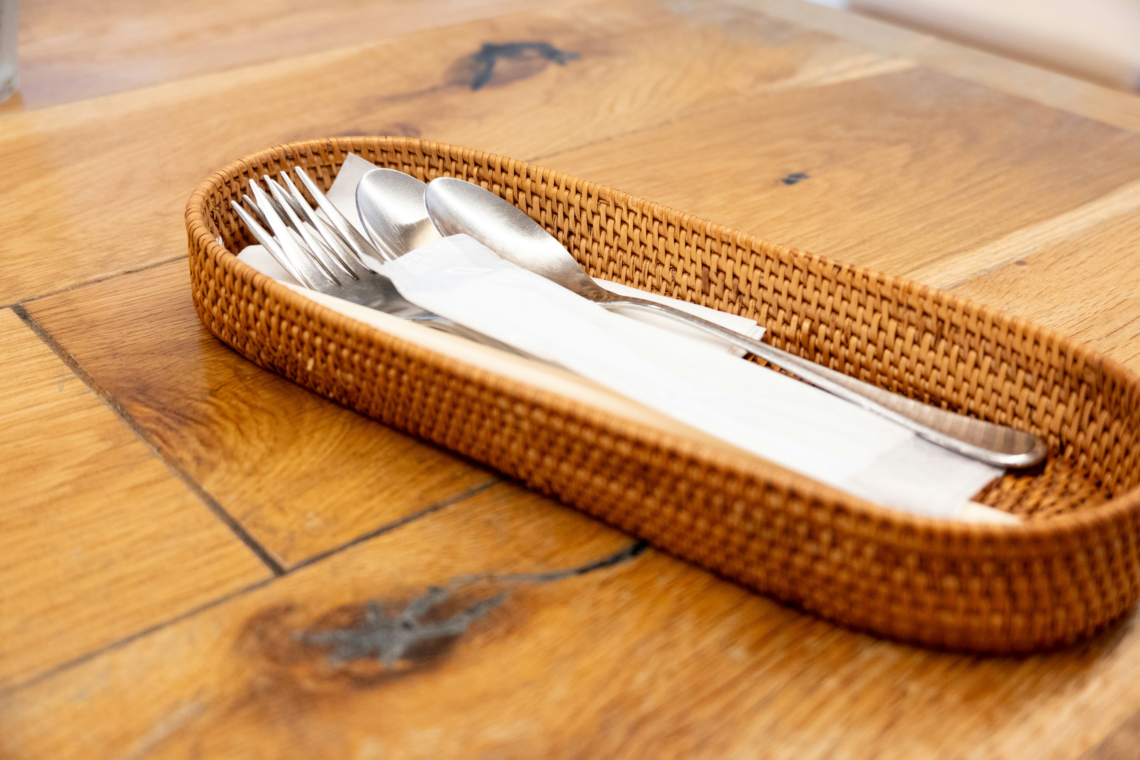 Cubiertos organizados en una cesta tejida sobre una mesa de madera