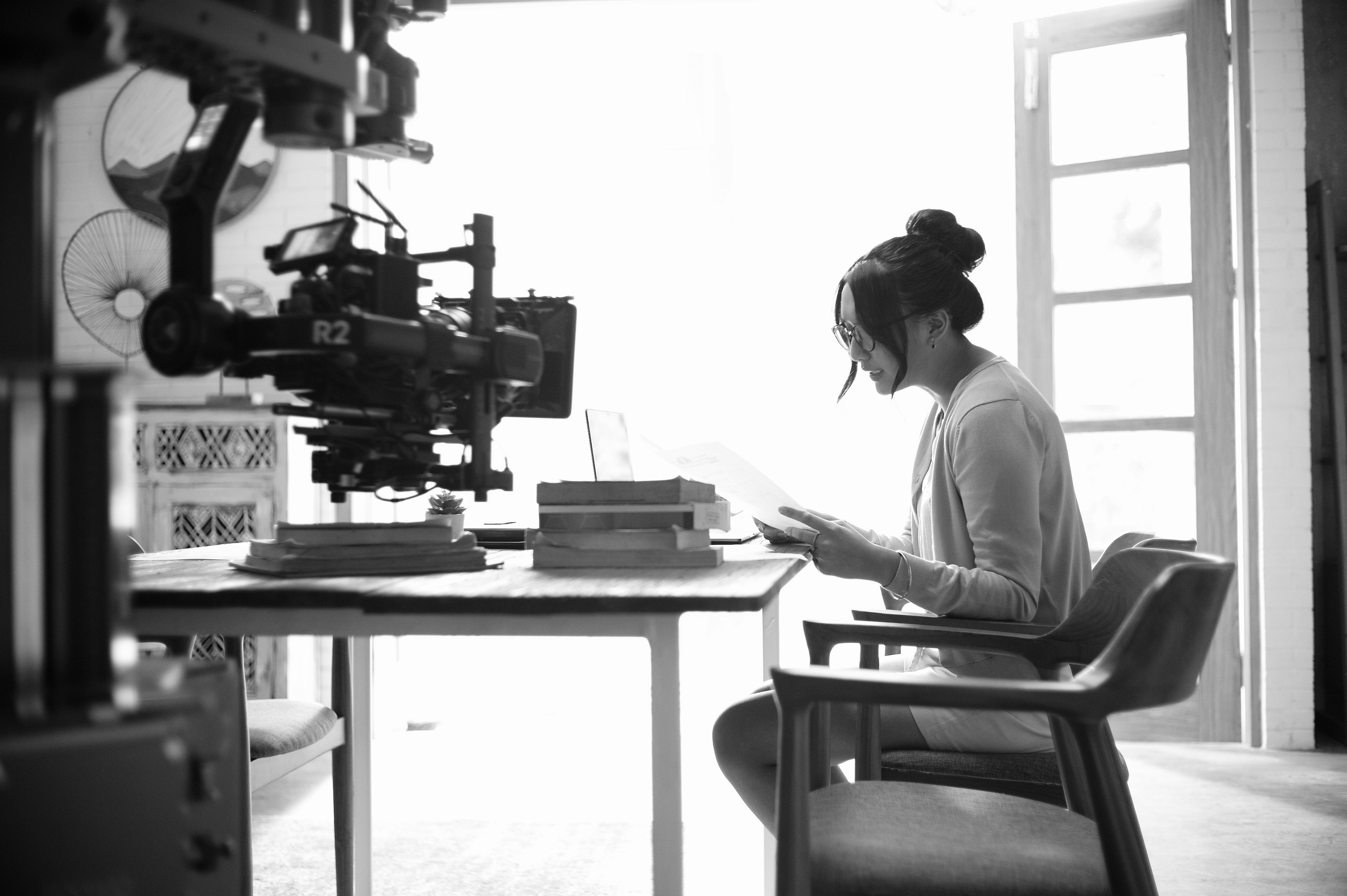 Imagen en blanco y negro de una mujer leyendo un libro frente a una cámara