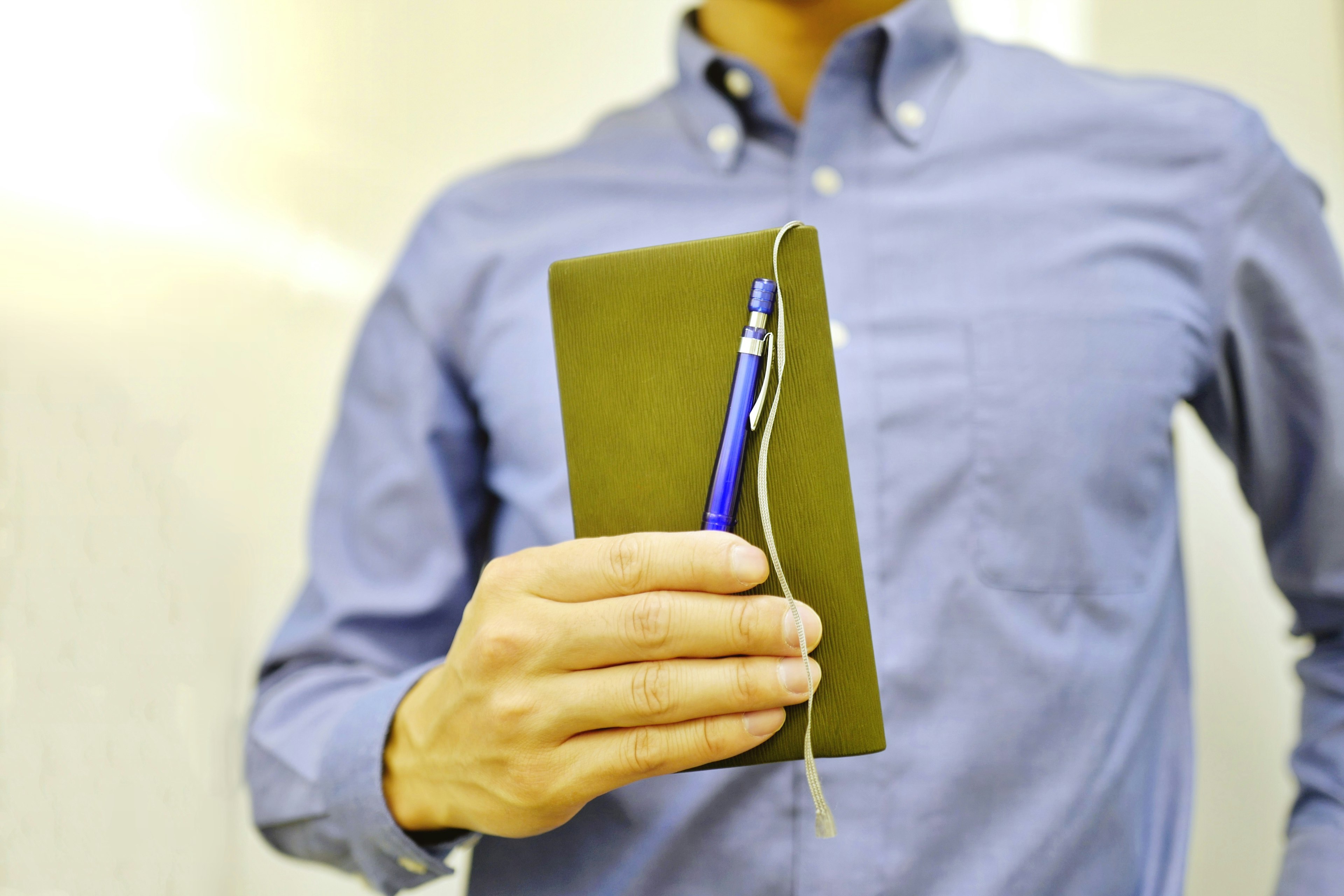 Seorang pria memegang buku catatan hijau dengan pulpen biru