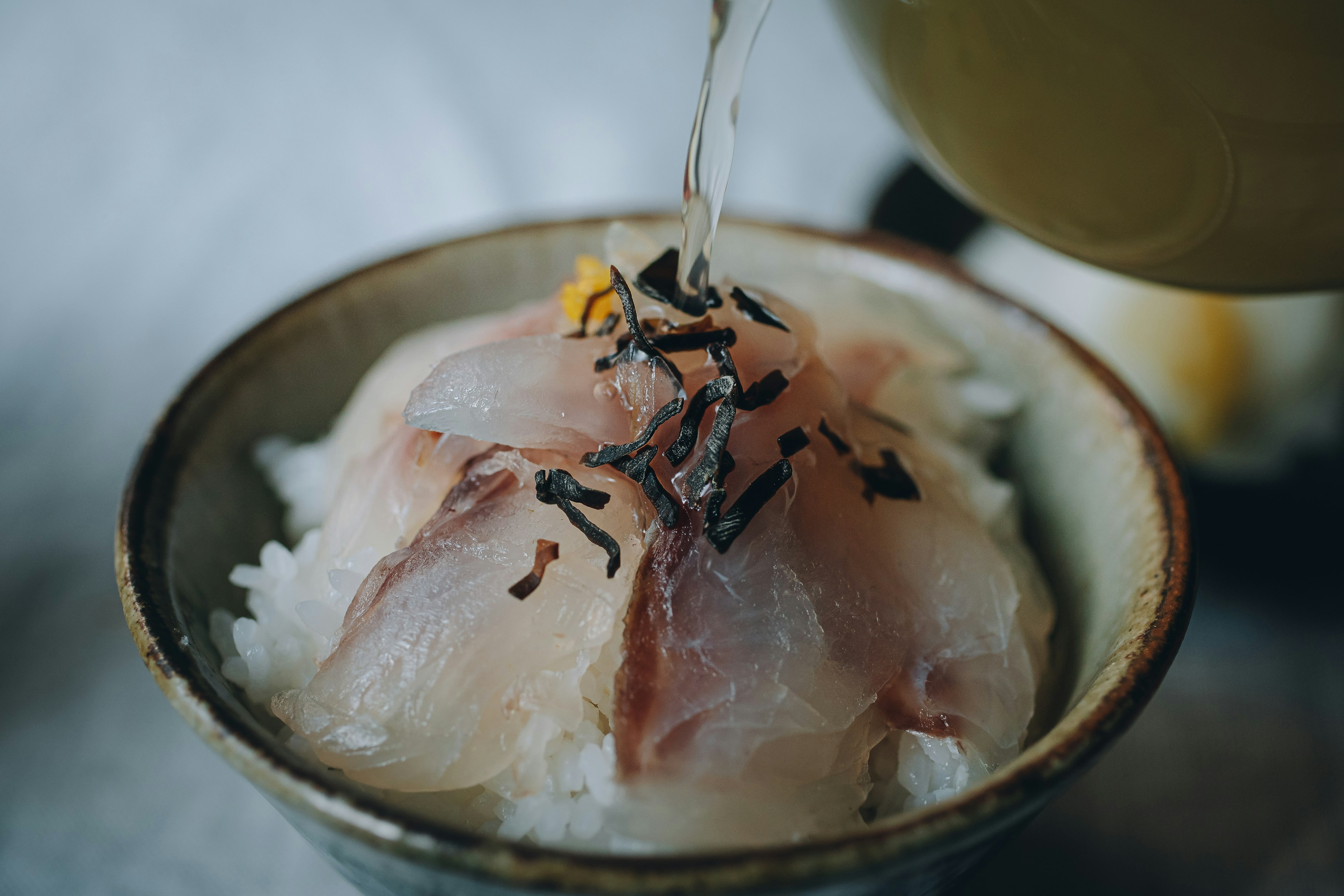 A bowl of rice topped with fresh sashimi being poured with hot broth