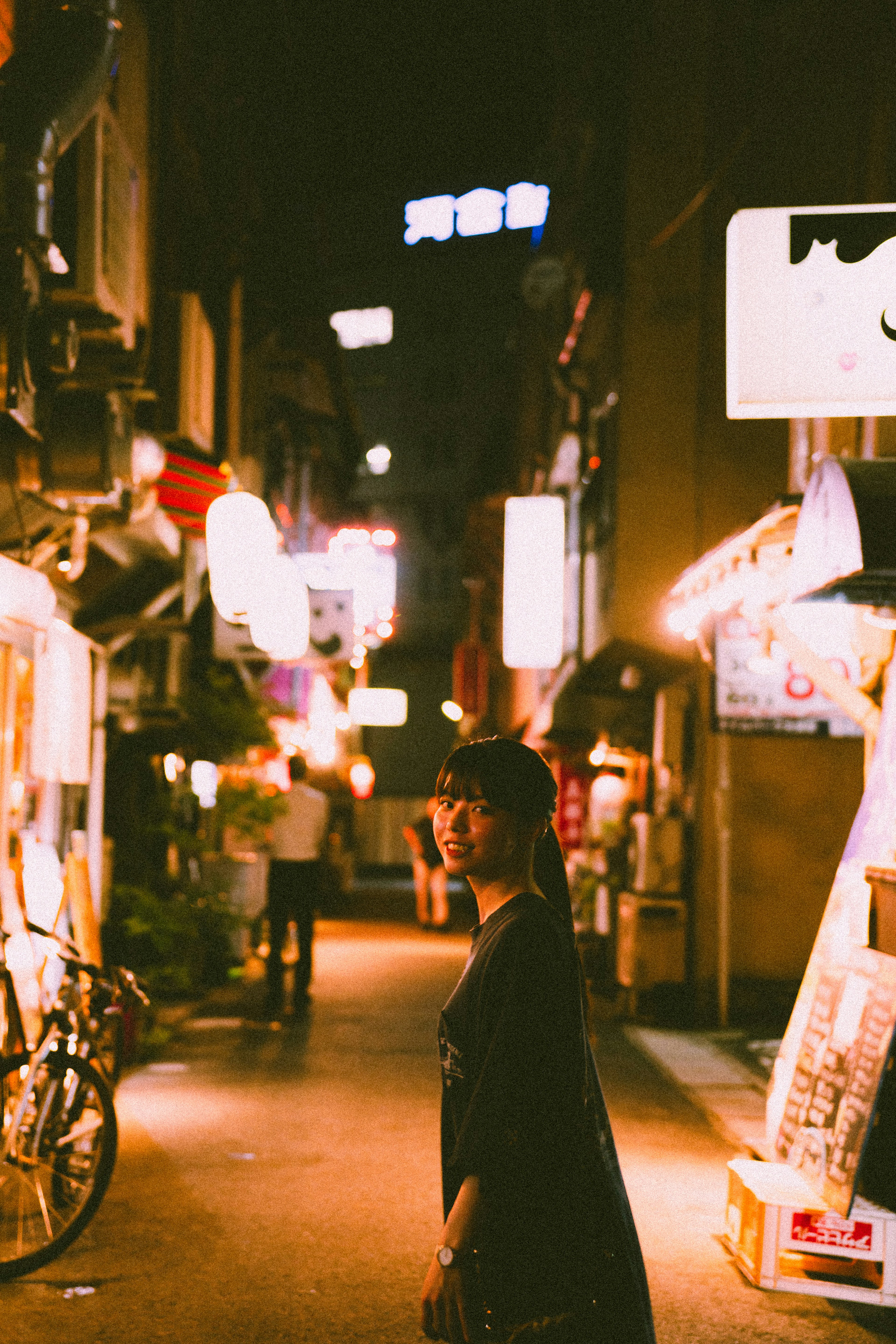 Persona caminando en un callejón estrecho iluminado por letreros brillantes por la noche