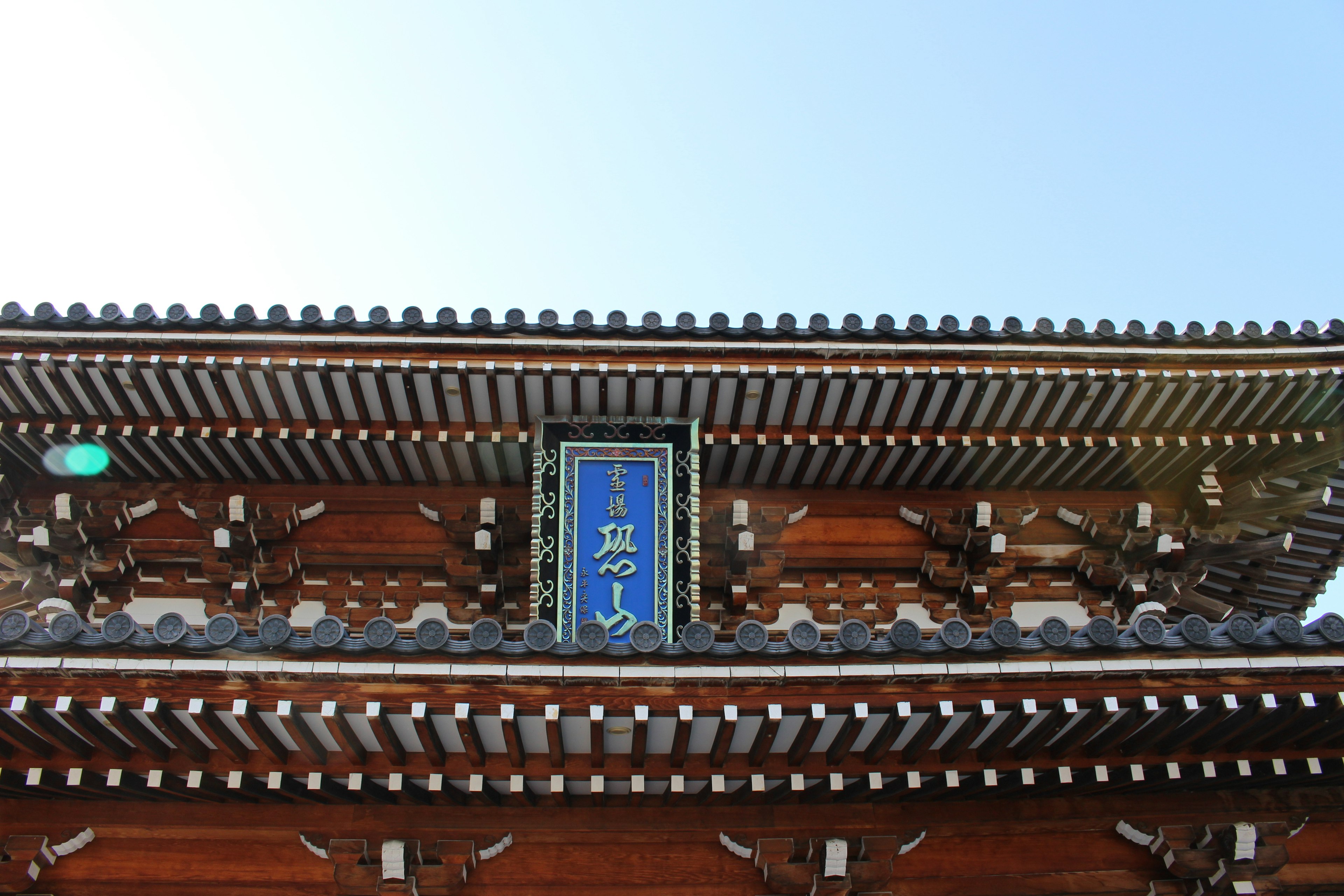 Traditional Japanese architectural gate with intricate details and a blue sign at the top