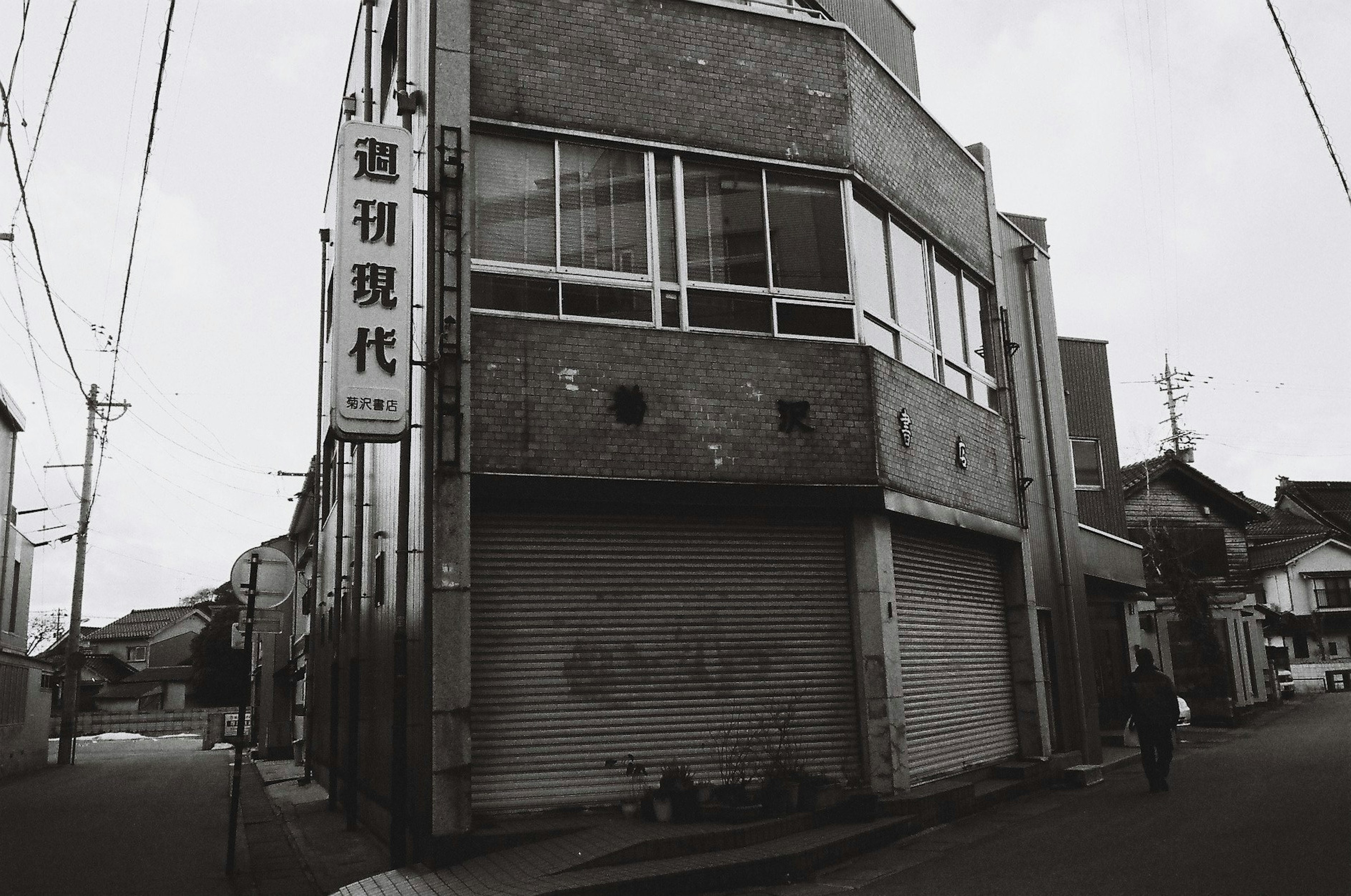 Ein graues Gebäude an der Ecke einer alten Straße mit Fenstern und einem Rollladen, typisch für die japanische Architektur