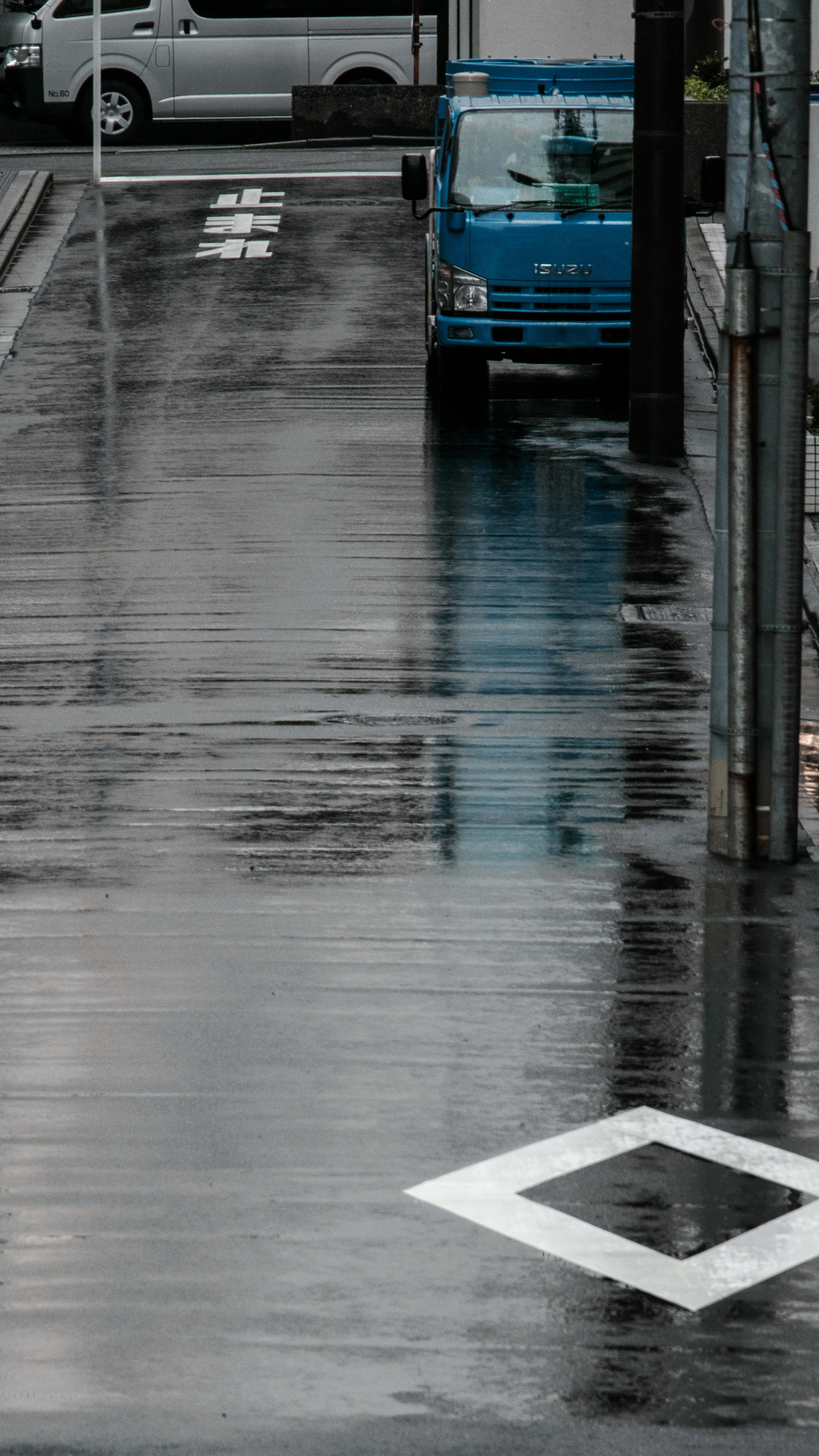 Wet street scene featuring a blue truck and reflective pavement