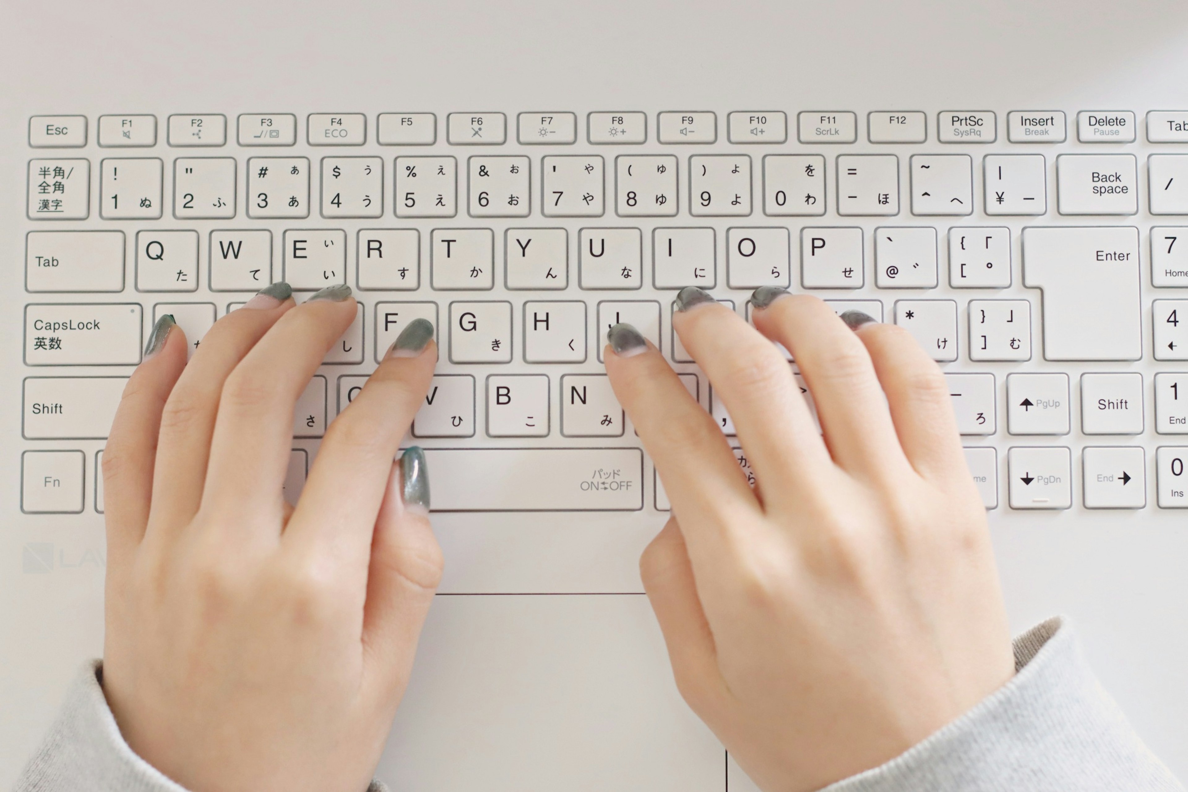 Hands typing on a white keyboard with gray nail polish