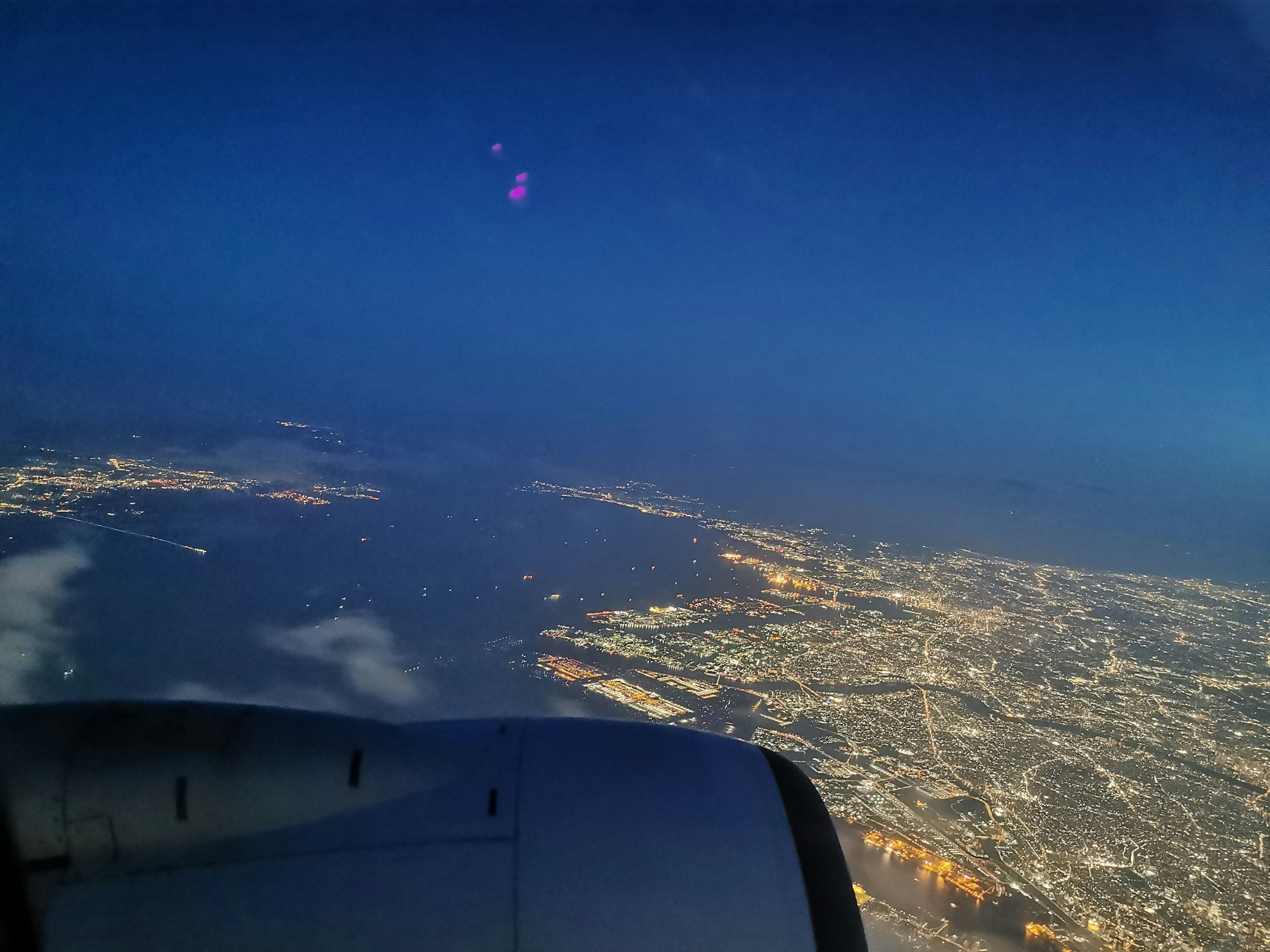 Vista notturna della città da un finestrino dell'aereo Parte del motore visibile con luci cittadine