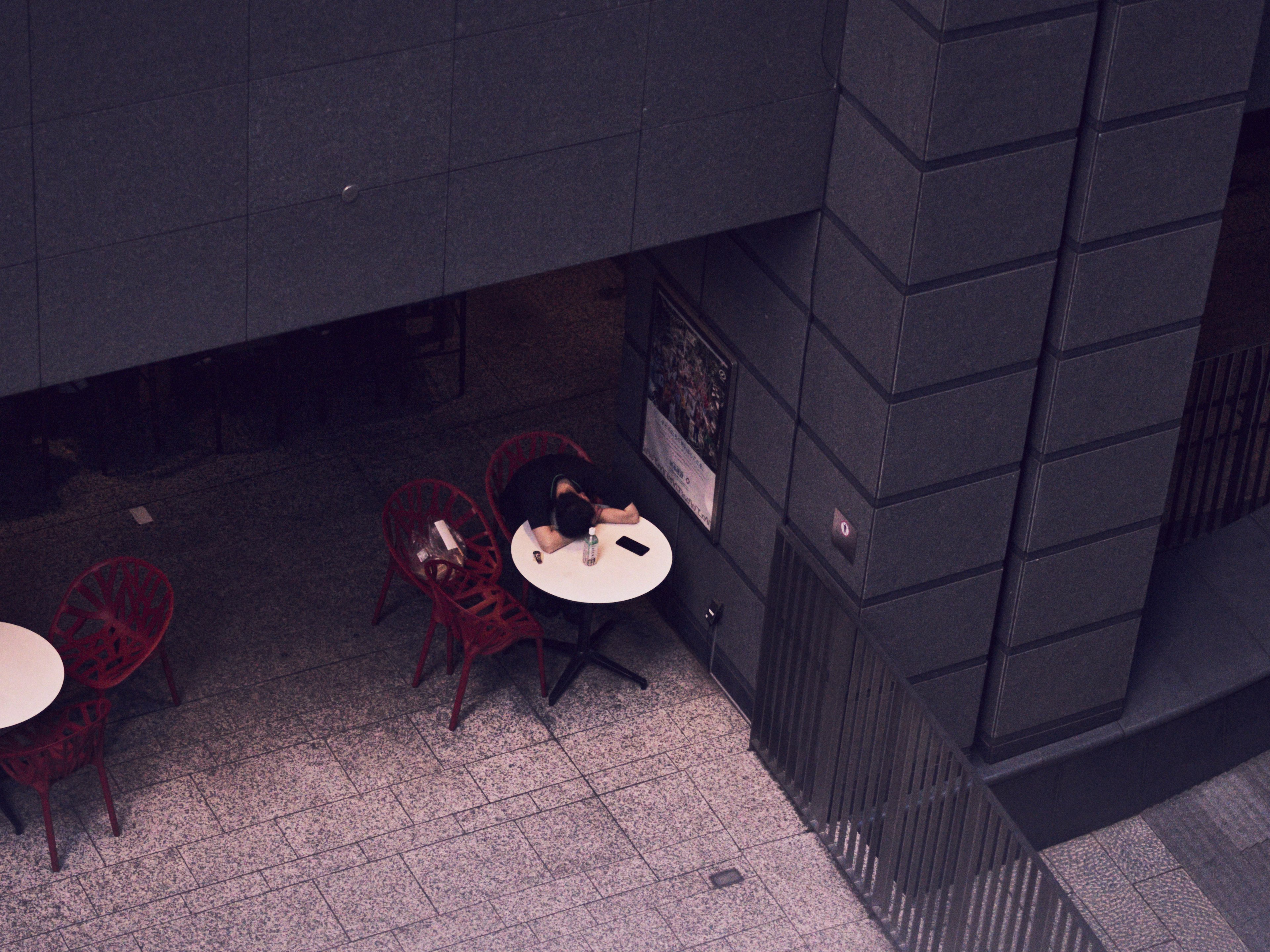 A café scene with a person dining at an outdoor table surrounded by red chairs