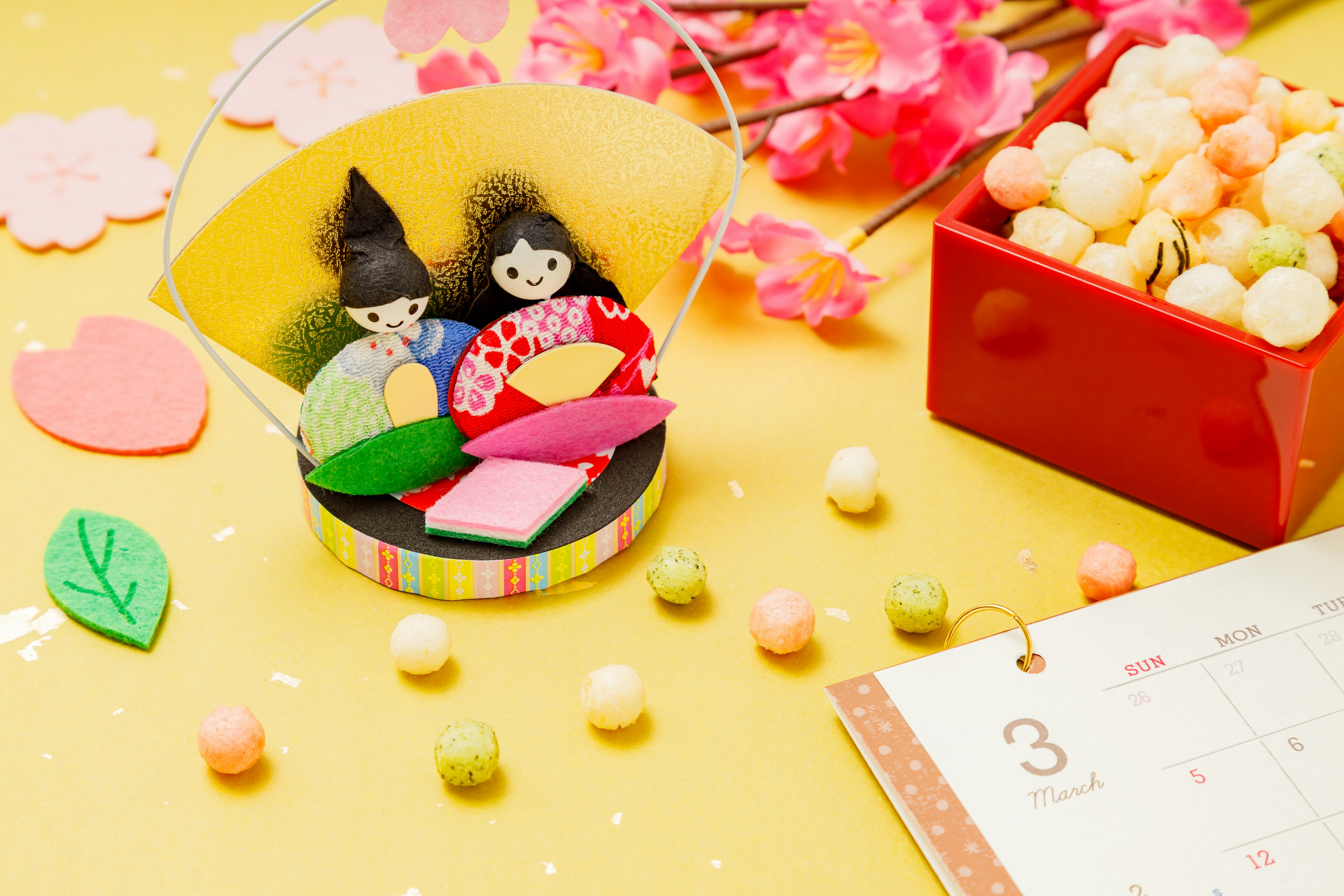 Colorful Hina dolls with traditional sweets on a bright yellow background