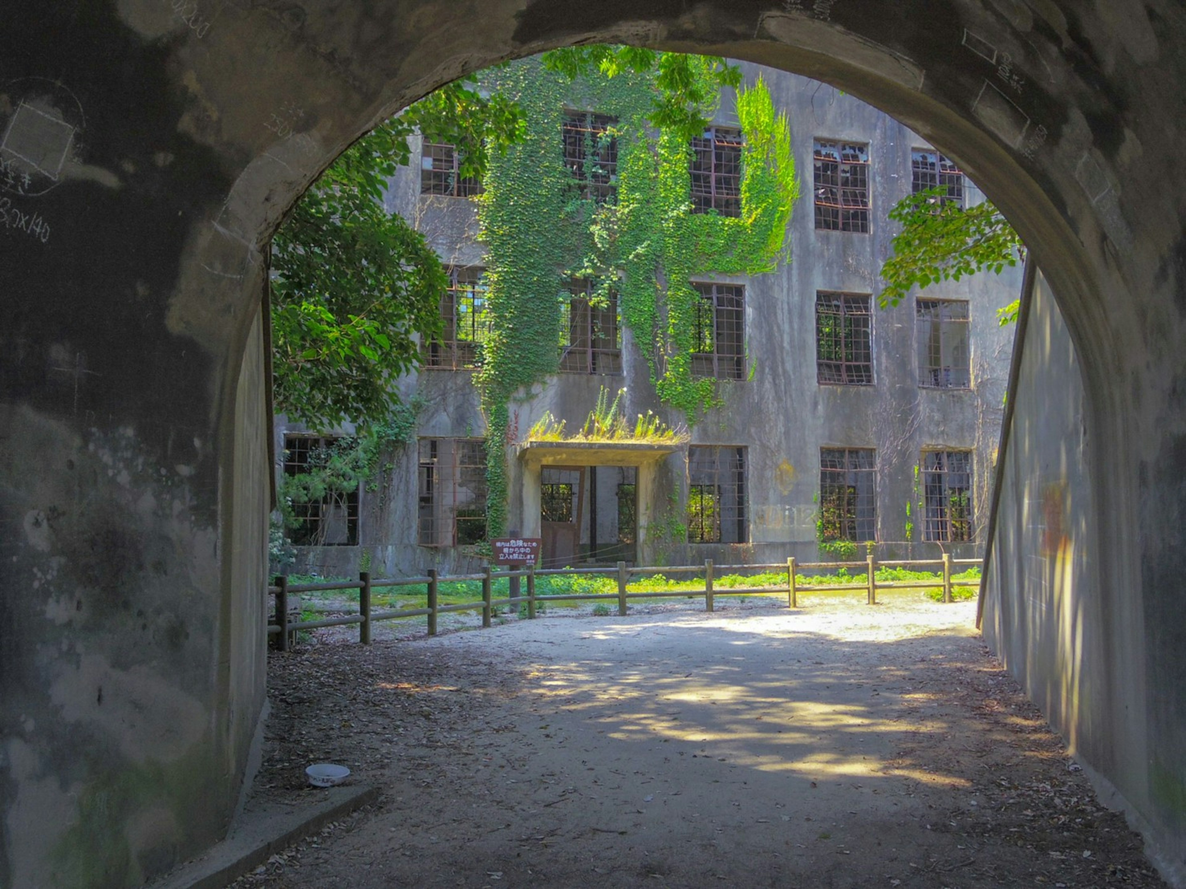 View through an archway of an old building covered in greenery with large windows