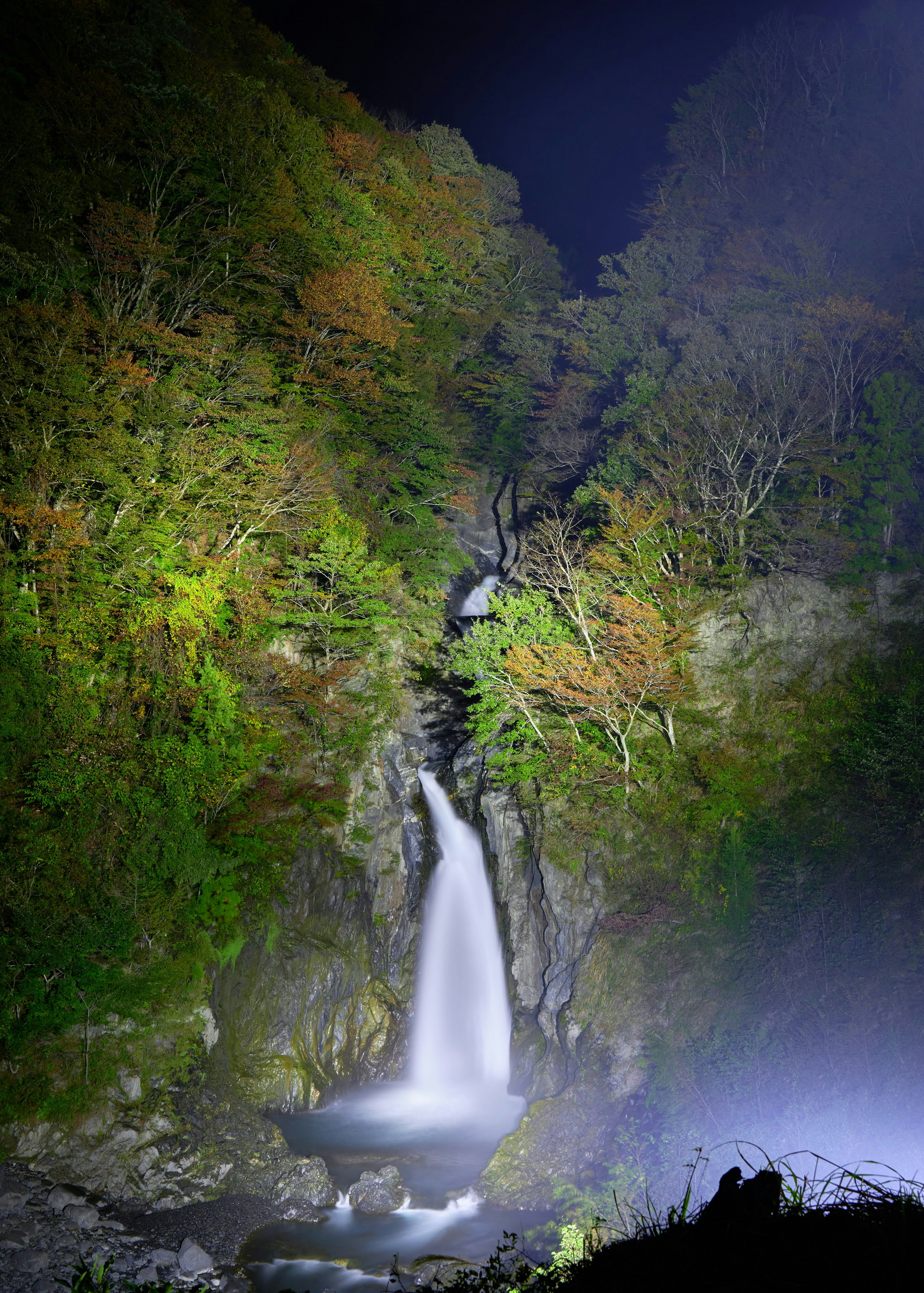 Una bellissima cascata illuminata di notte in un paesaggio verdeggiante