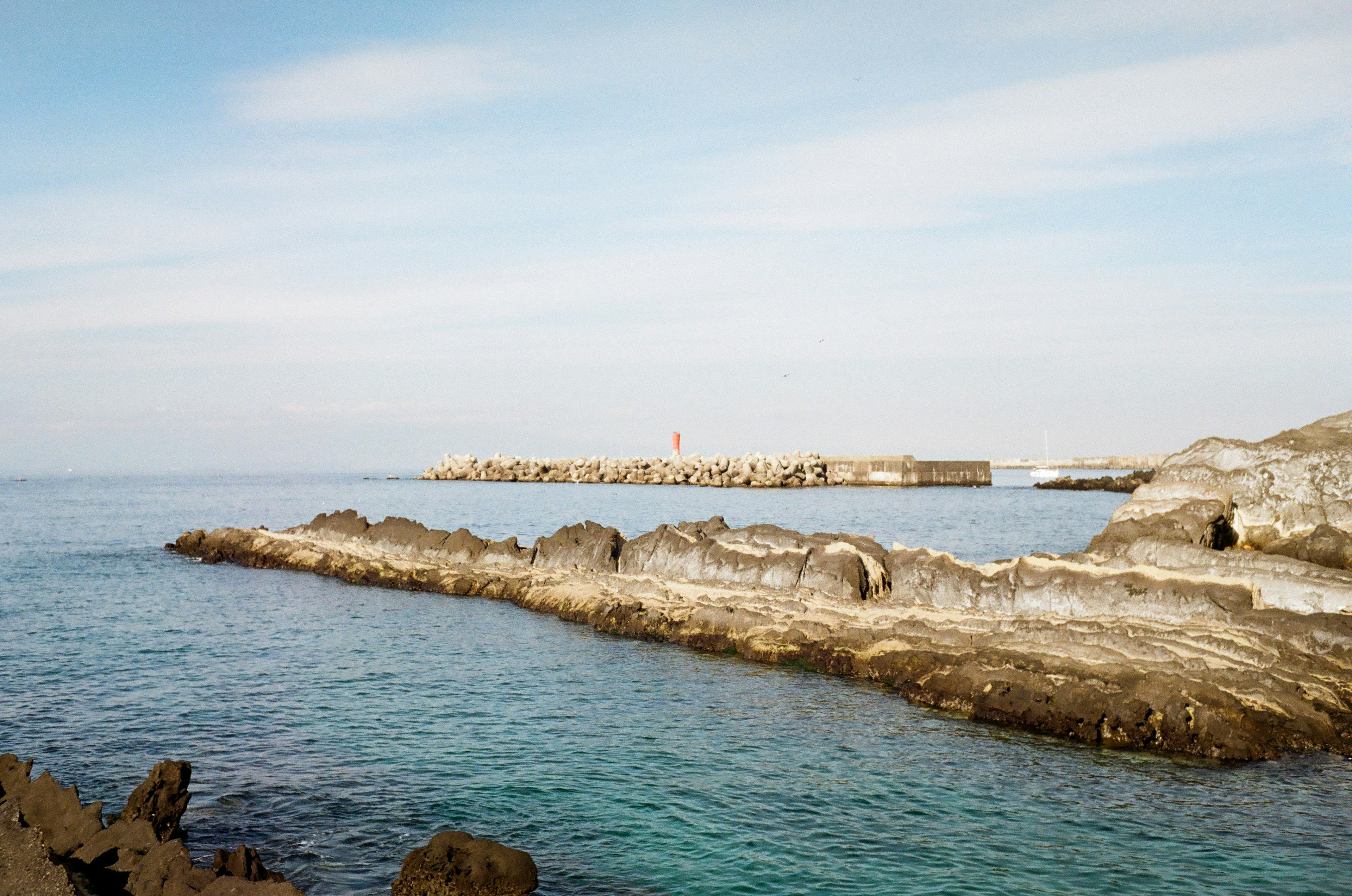 Mar calmado y paisaje rocoso con un muelle desgastado al fondo