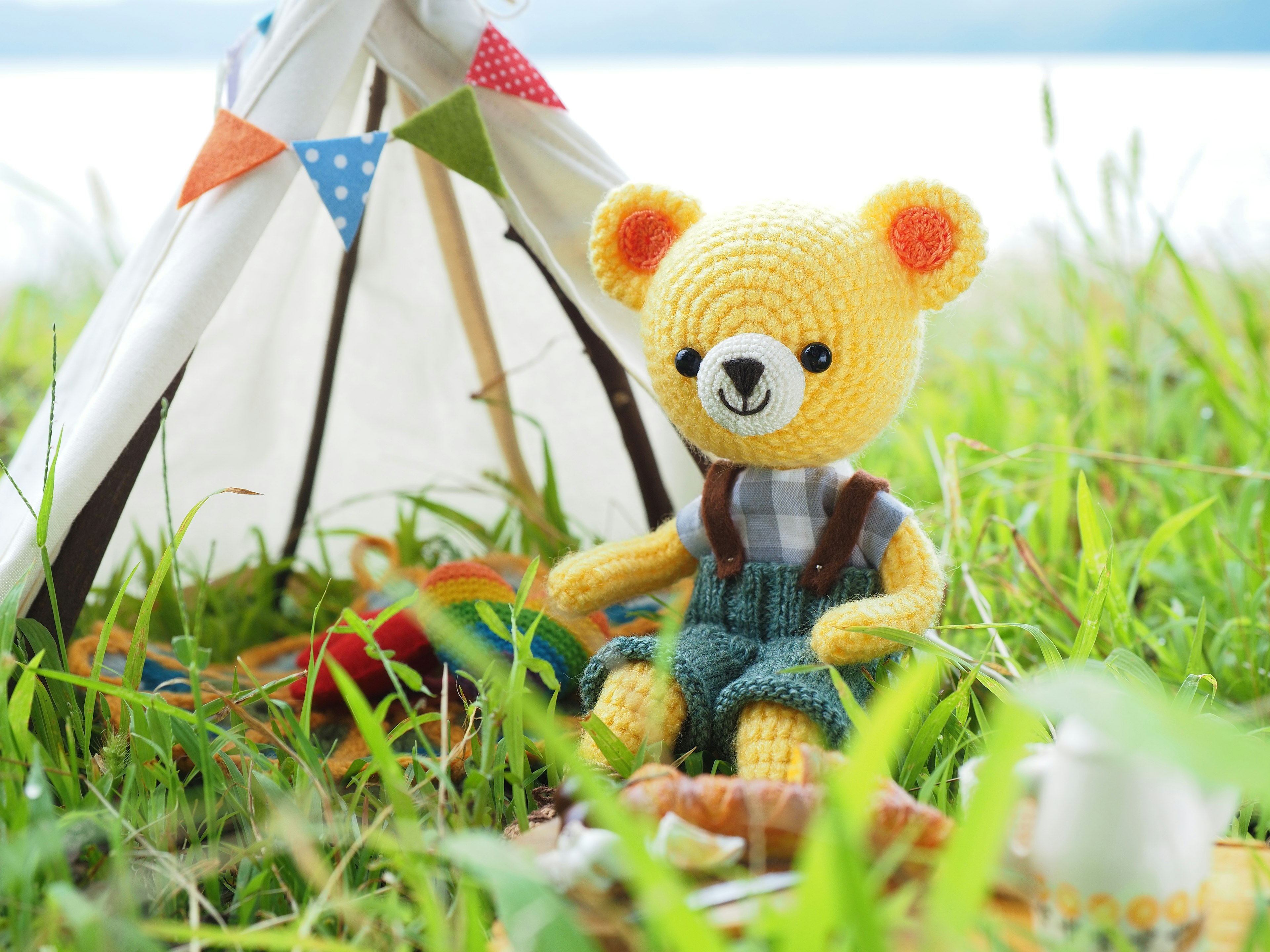 A yellow teddy bear sitting in front of a tent amidst green grass