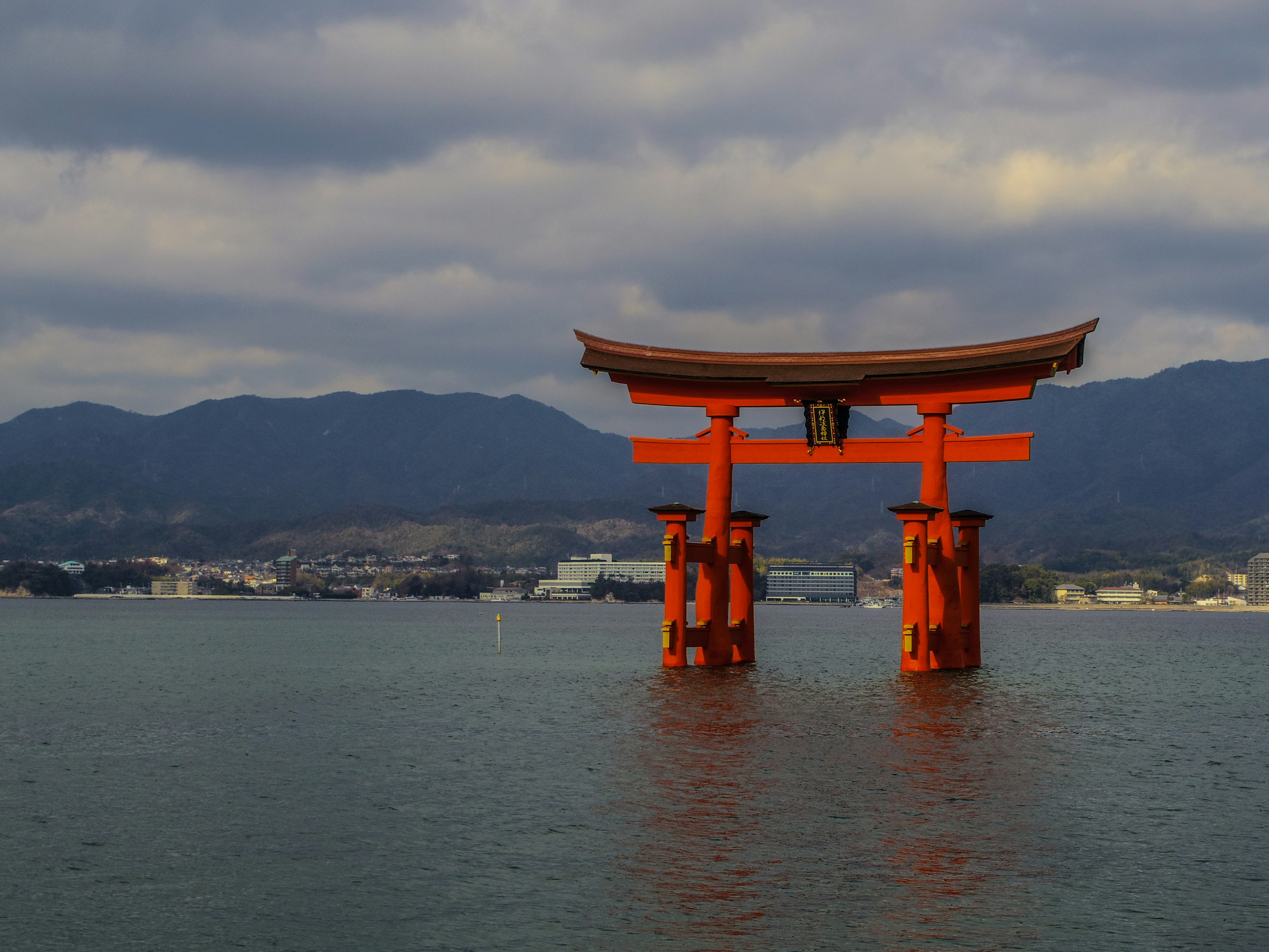 Torii naranja flotando en el mar con montañas al fondo