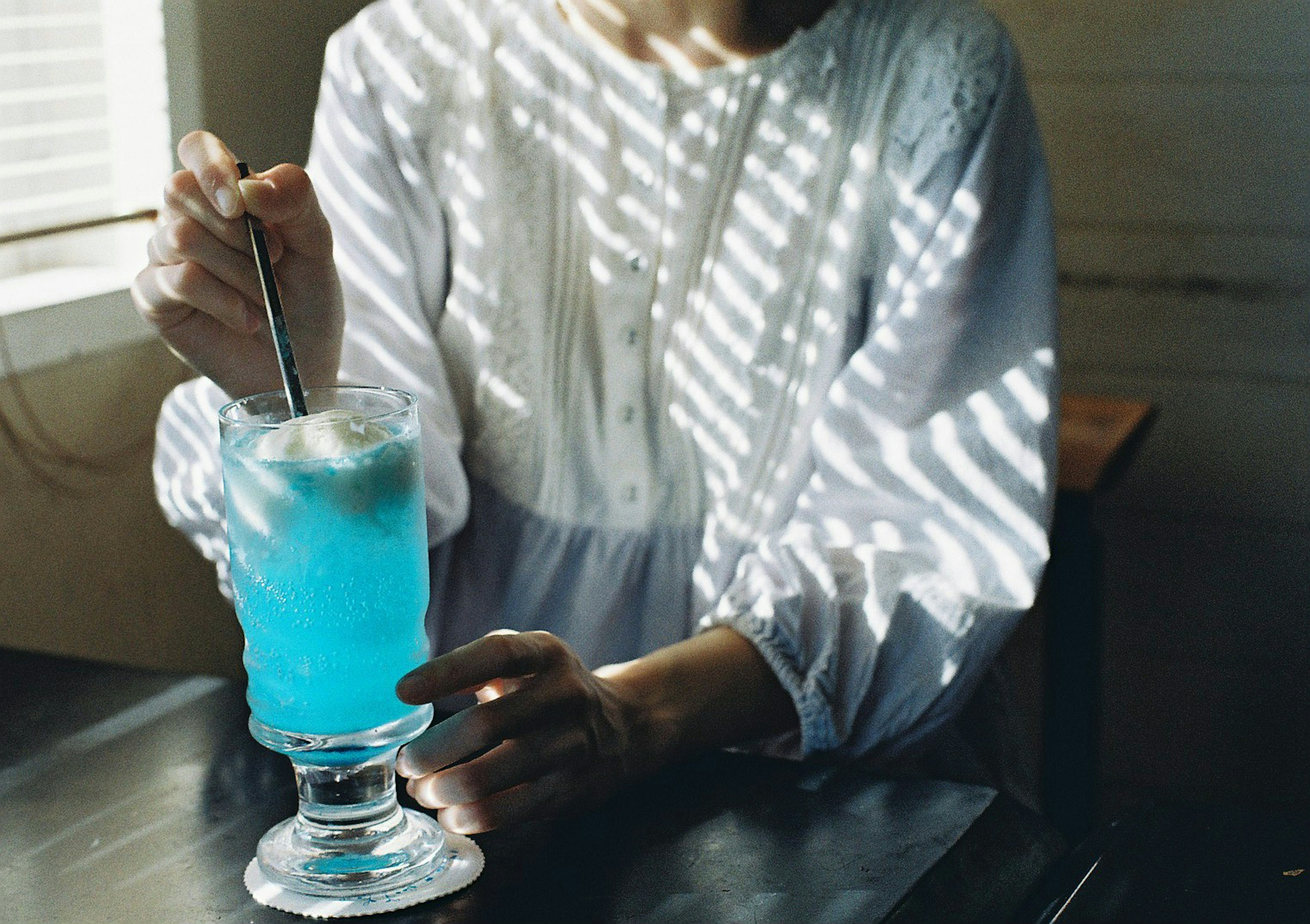 A woman's hand holding a blue drink with striped light