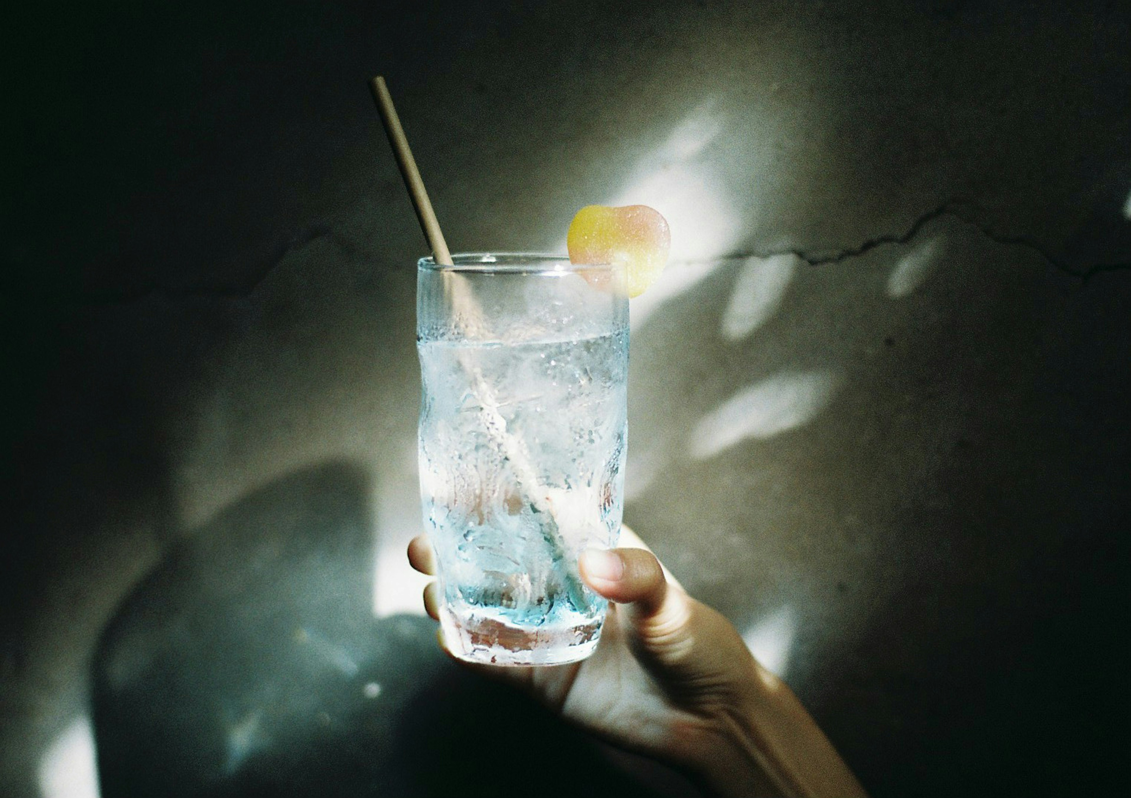 A hand holding a clear glass filled with ice and a slice of lemon