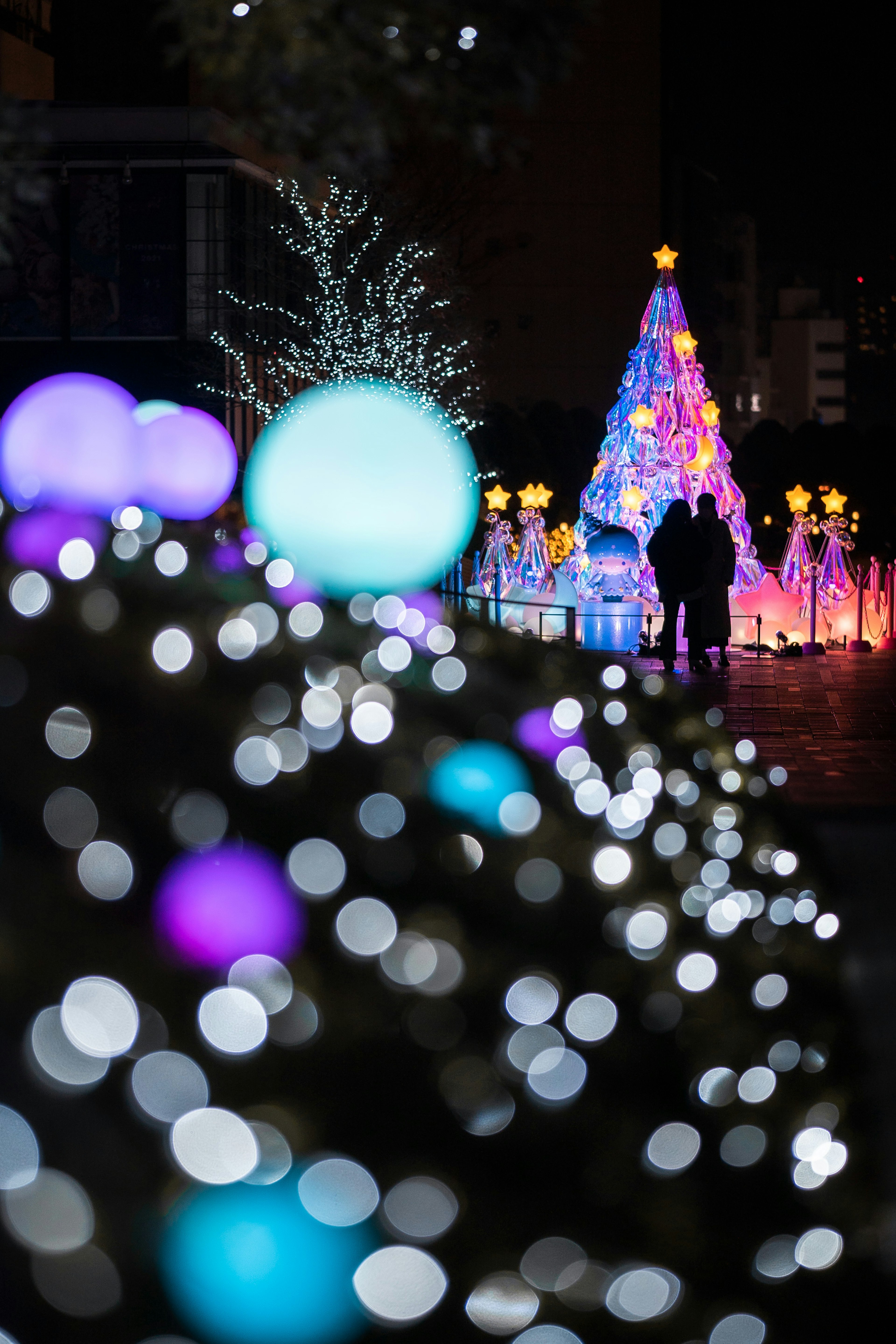 Pohon Natal berwarna-warni yang diterangi malam dengan dekorasi latar depan yang kabur