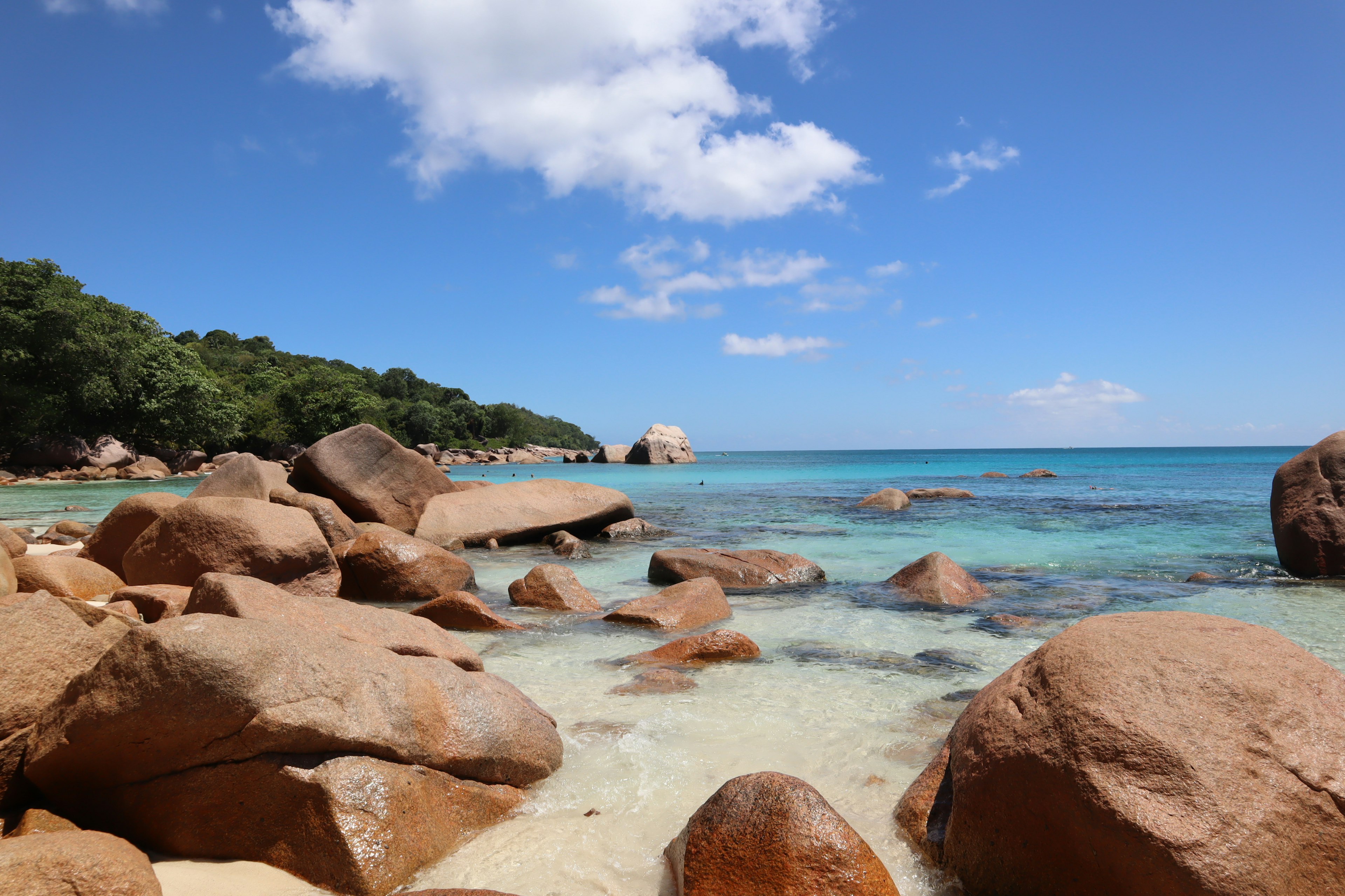 Vista panoramica della spiaggia con acqua blu chiara e nuvole bianche grandi rocce sparse lungo la riva