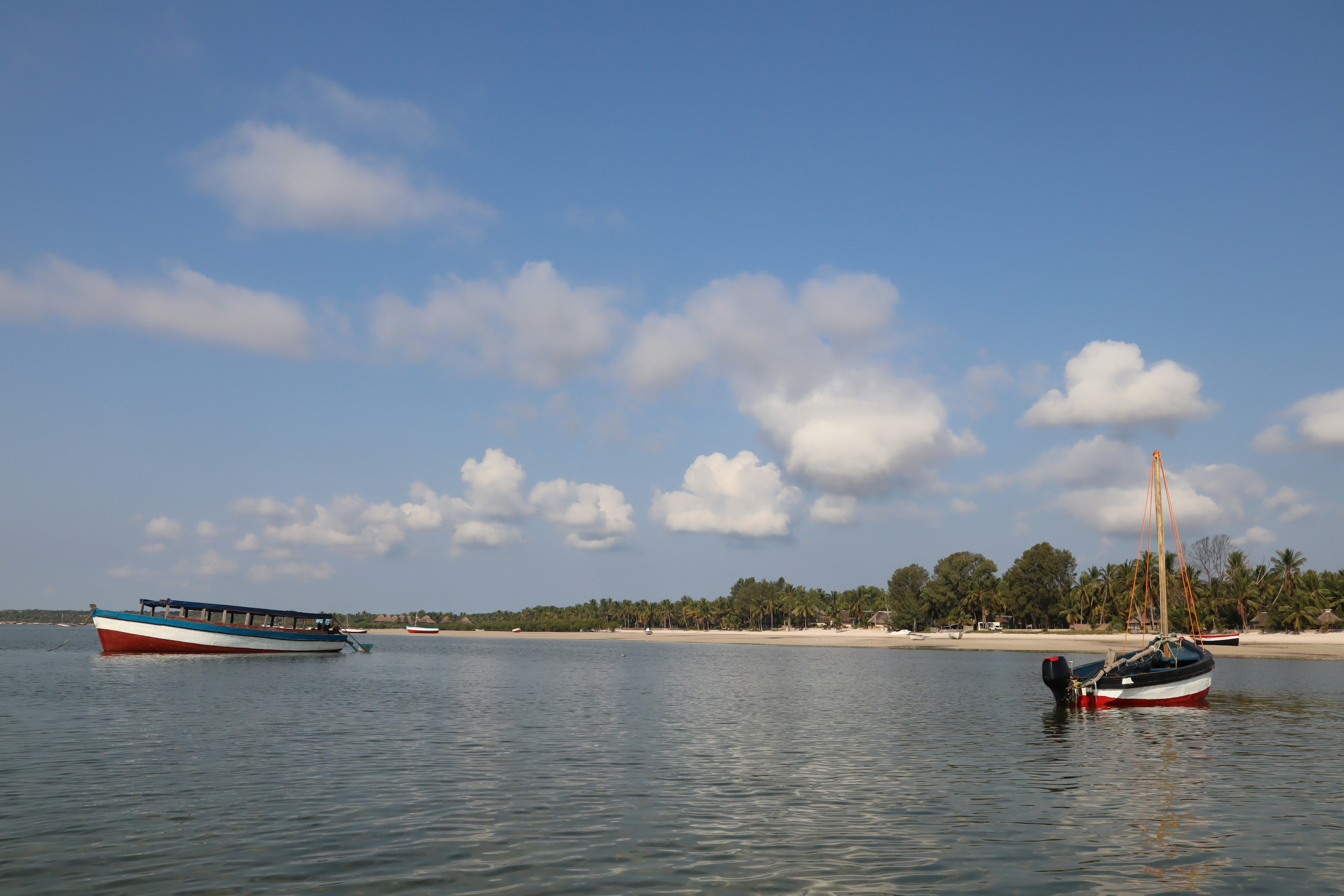 ทิวทัศน์ทะเลที่เงียบสงบพร้อมเรือสองลำในน้ำสงบใต้ท้องฟ้าสีฟ้าและเมฆฟูฟ่อง