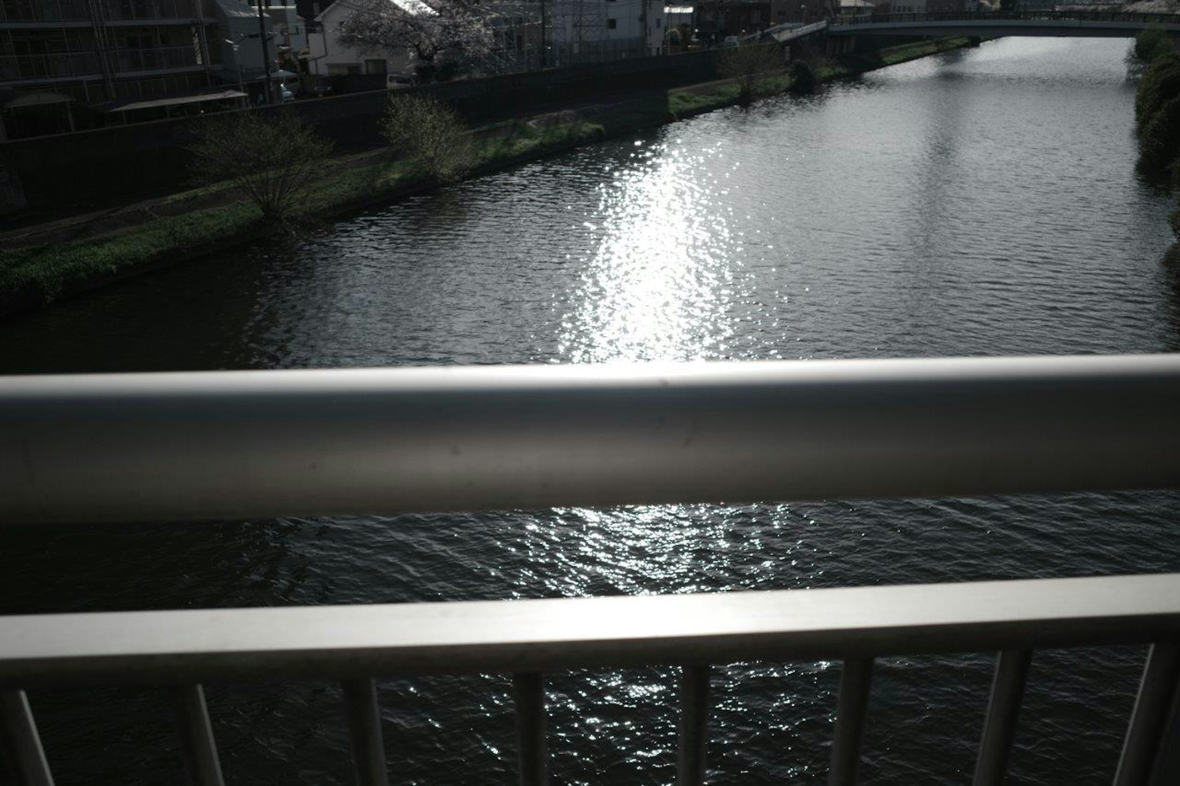 View of a river reflecting light with a bridge railing in the foreground