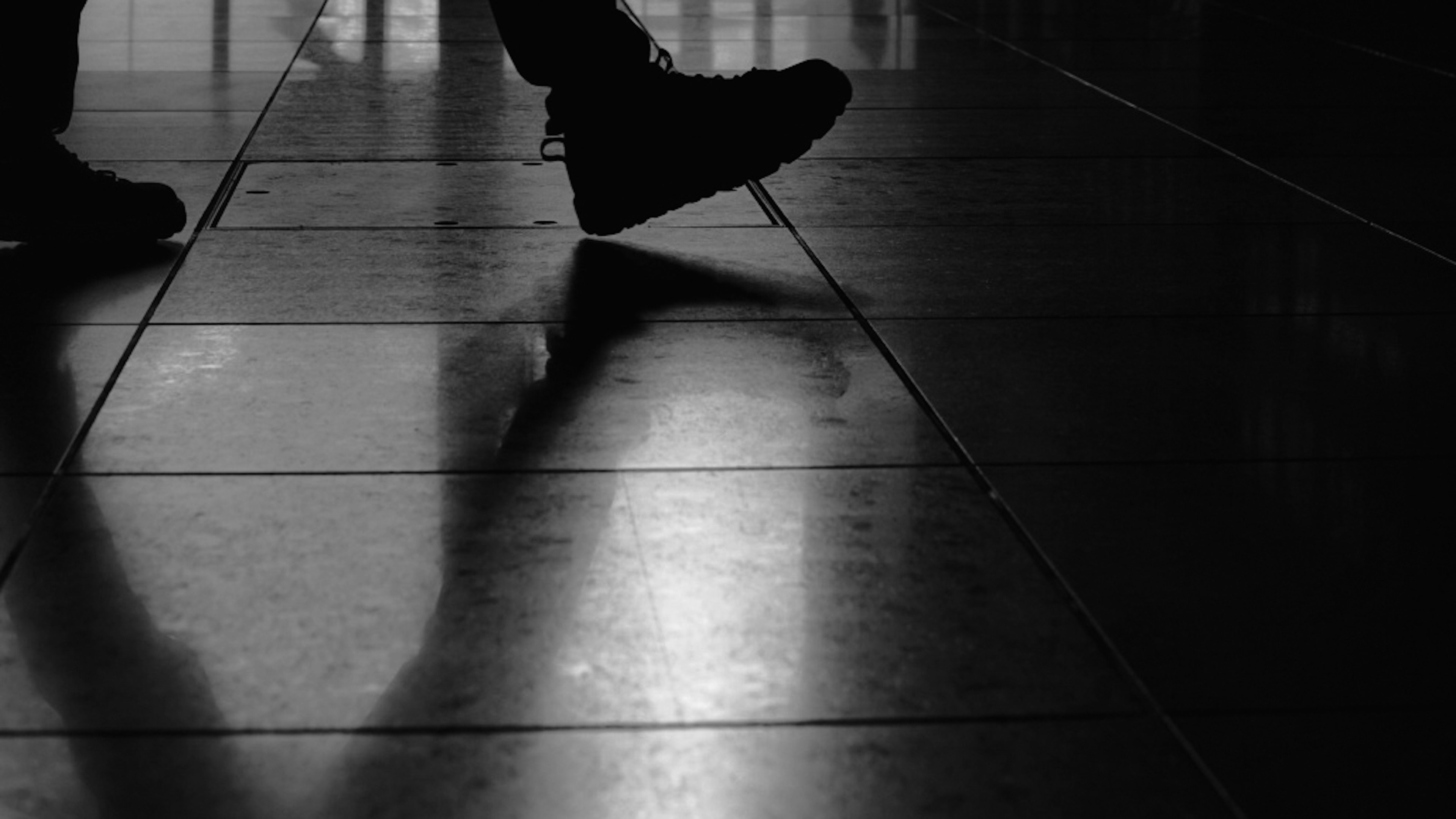 Silhouette of a person walking on tiled floor wearing black shoes