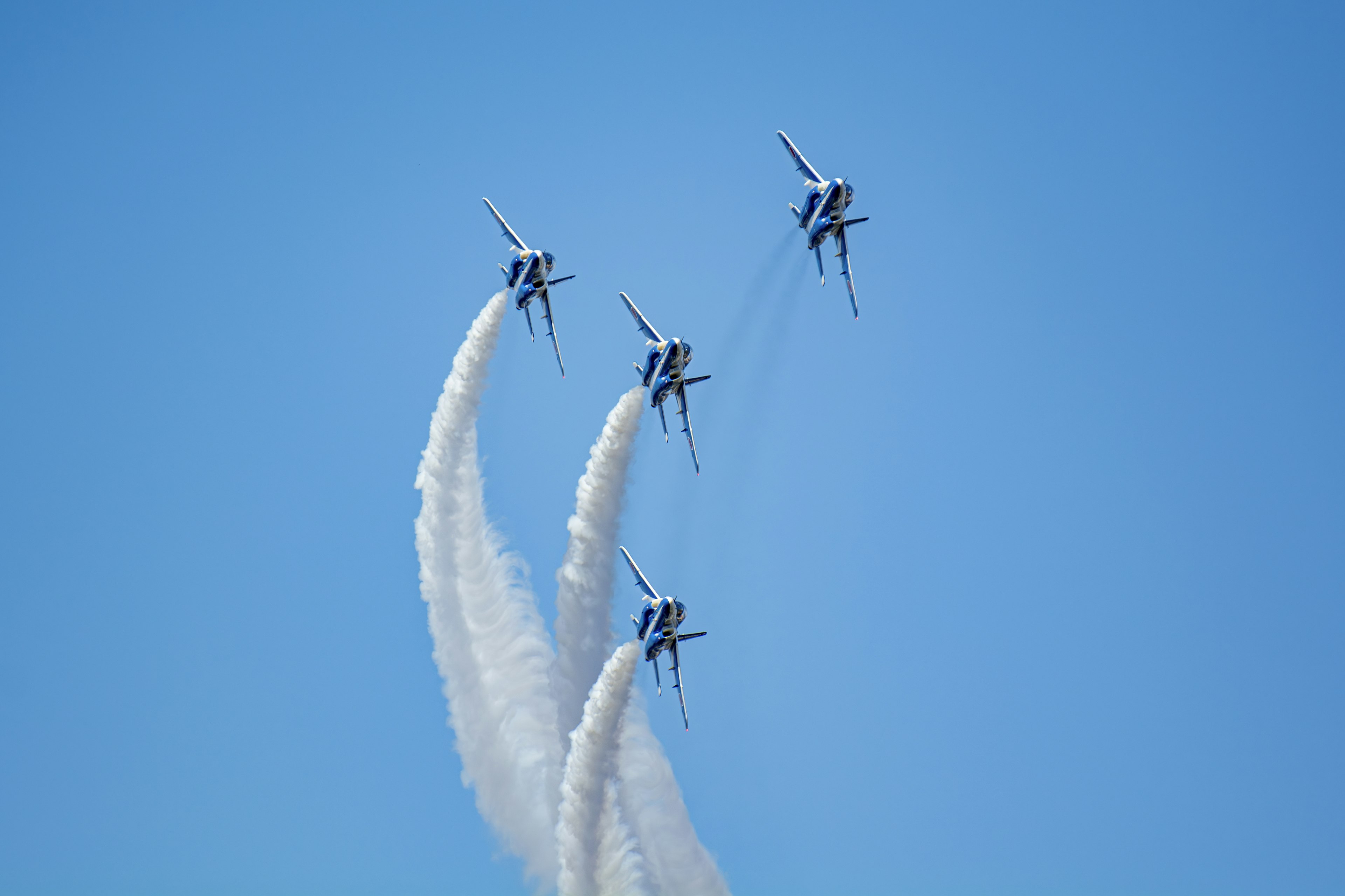 Four planes performing aerial maneuvers with white smoke against a blue sky