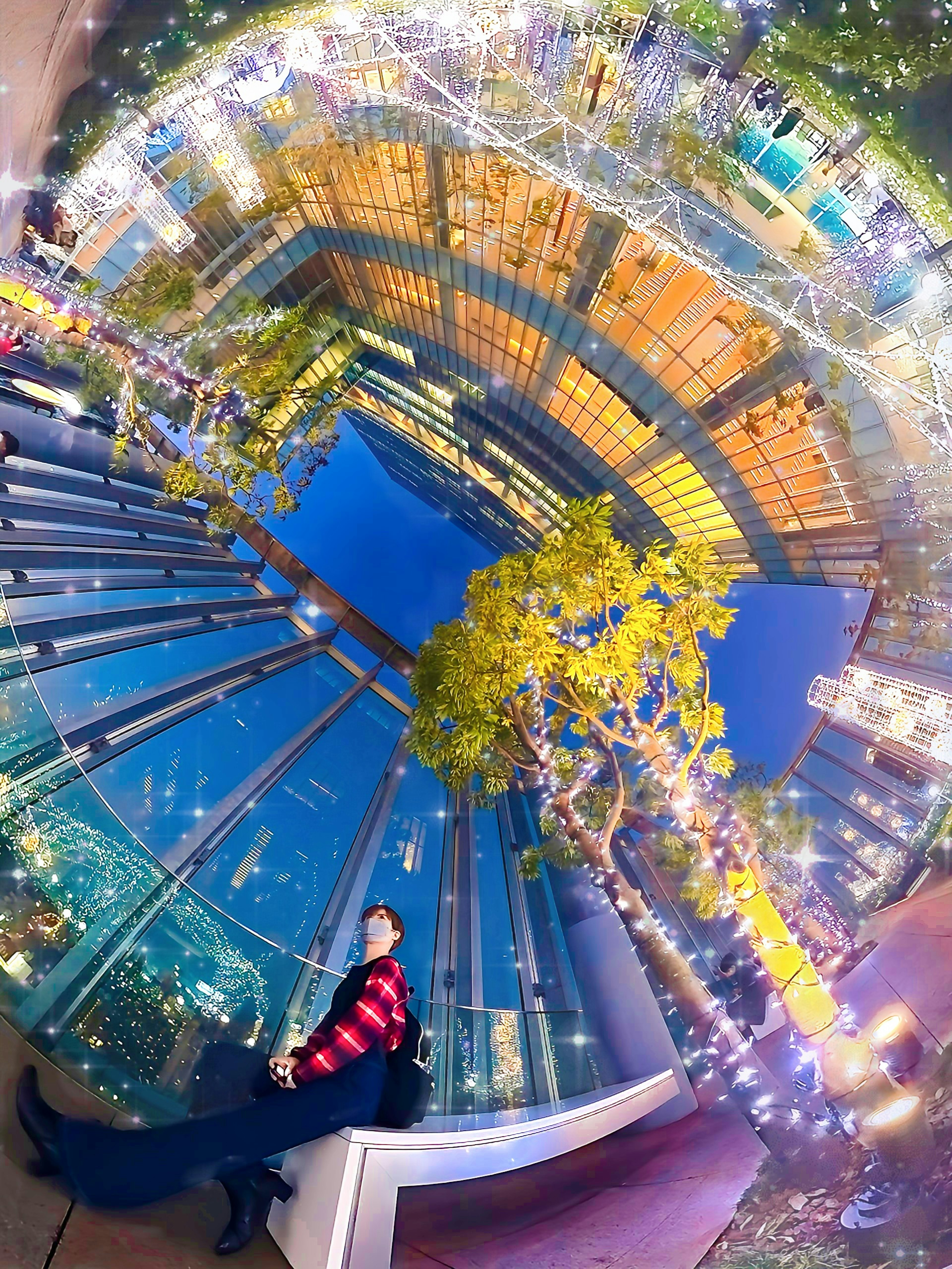 Una persona mirando hacia arriba a un paisaje urbano vibrante con luces brillantes y vegetación