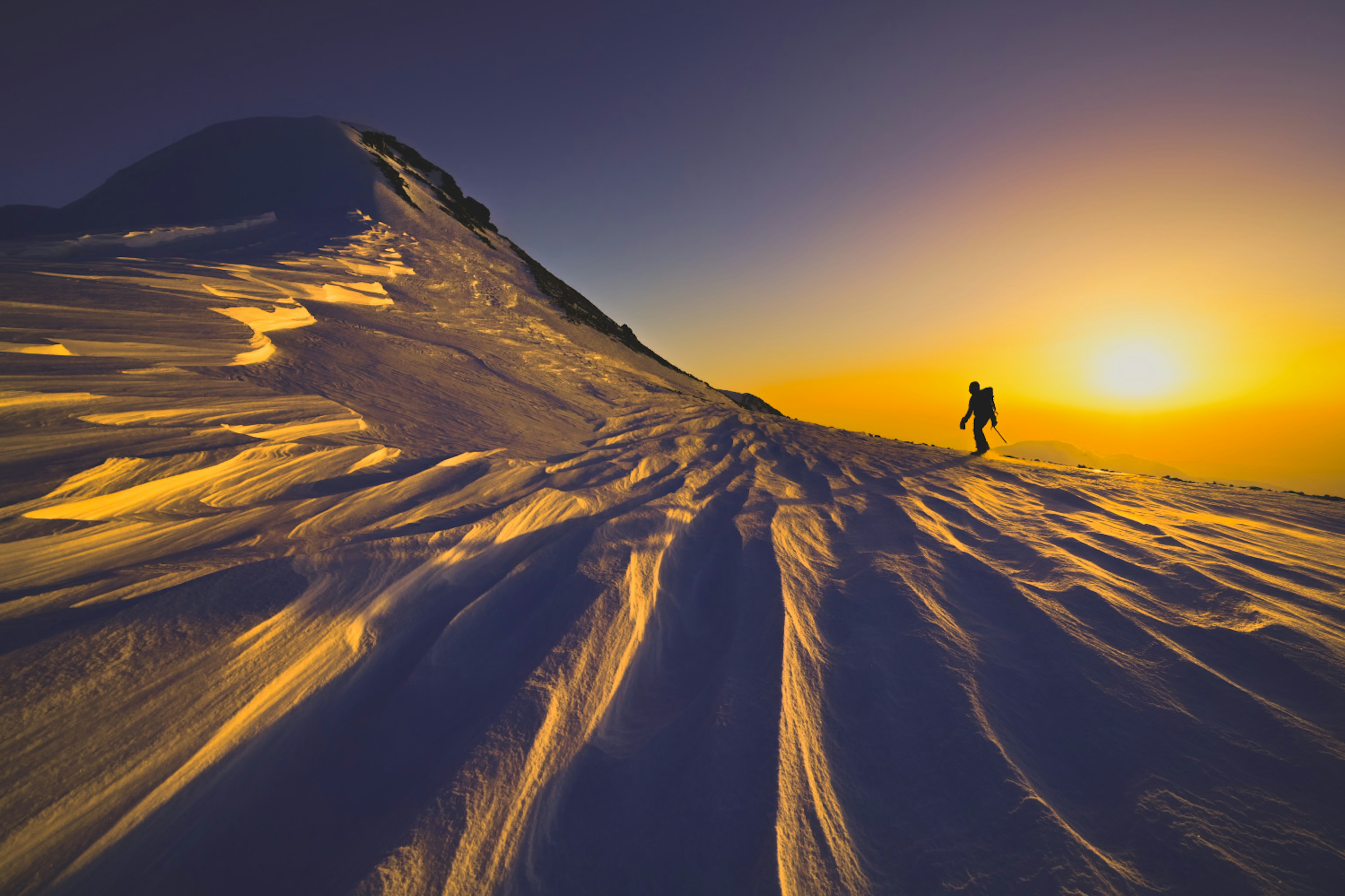 Bergsteiger, der einen verschneiten Berghang mit einem atemberaubenden Sonnenuntergang erklimmt