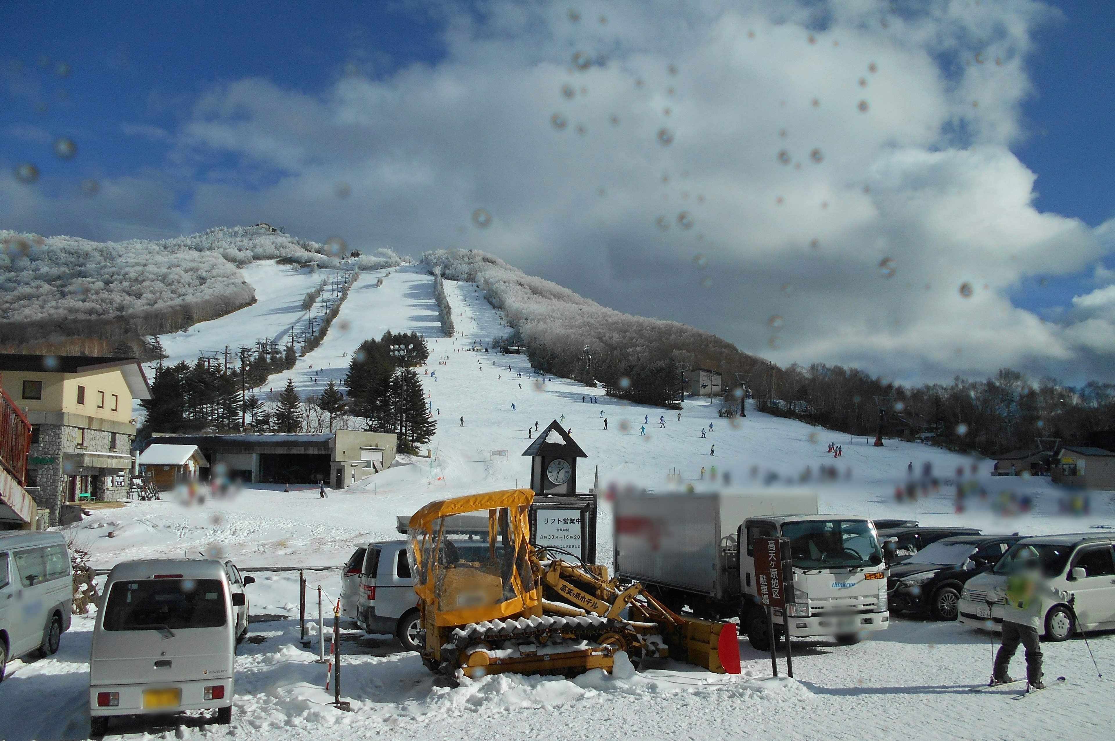 Snow-covered mountain with ski lift in the background parking lot with vehicles and snowplow