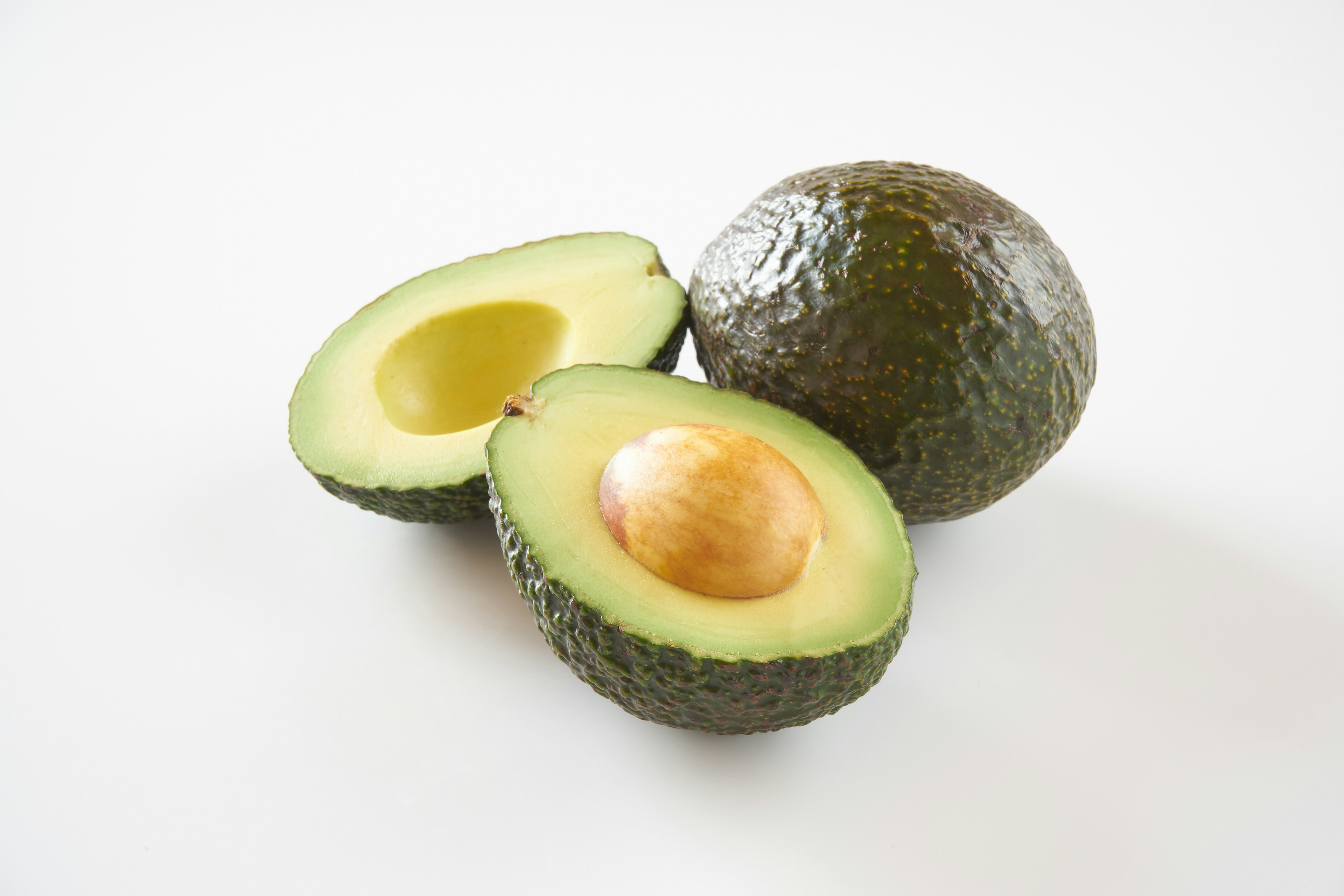 A halved avocado and a whole avocado on a white background