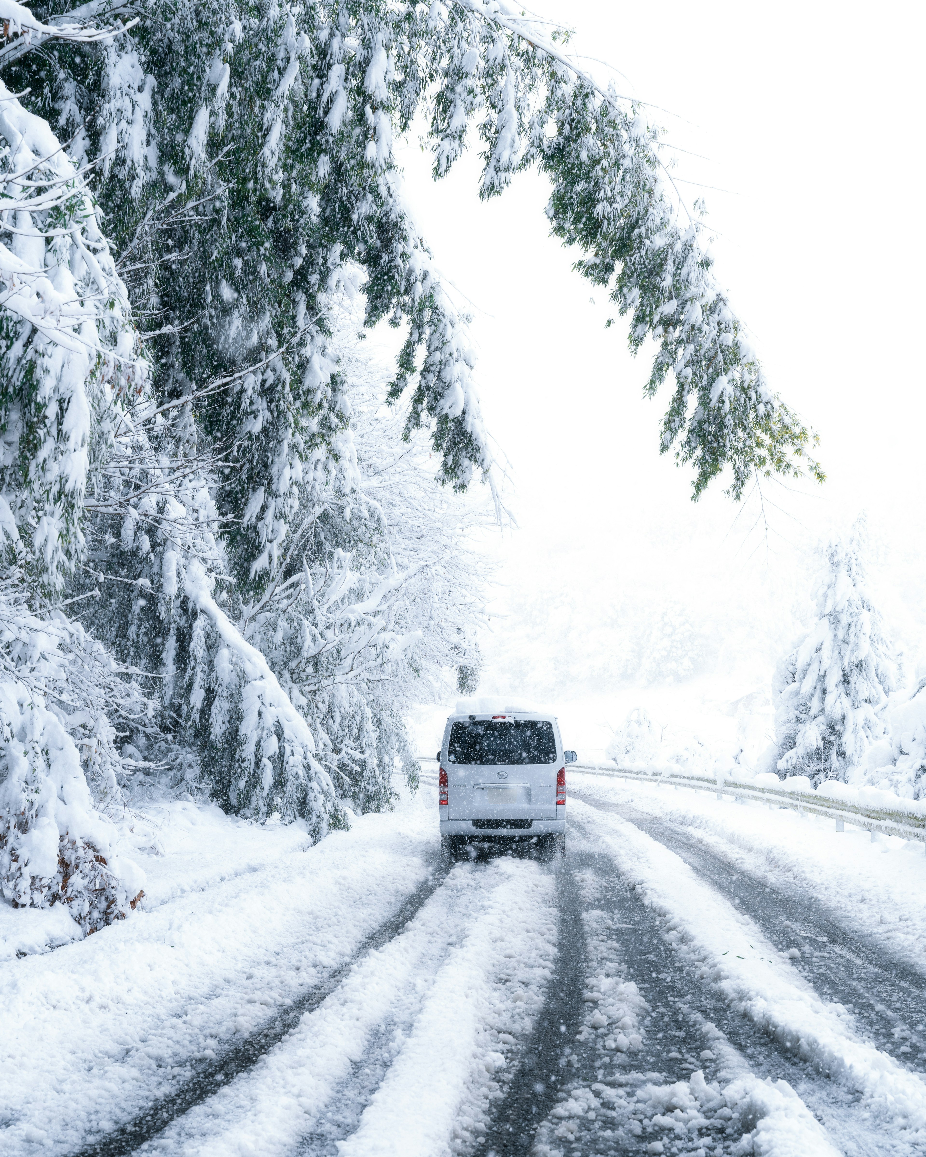 A vehicle driving on a snowy road surrounded by snow-covered trees