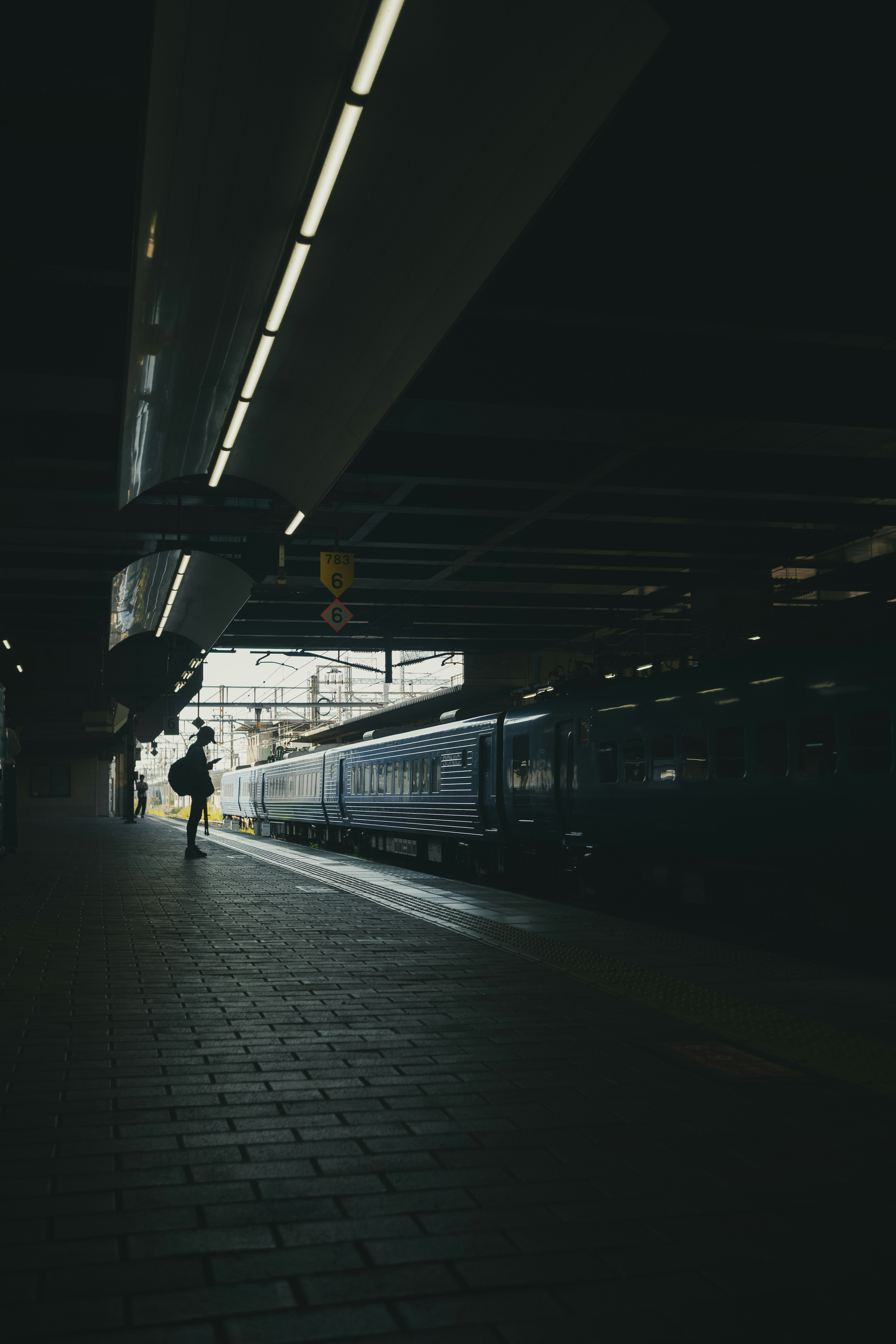 暗い駅のプラットフォームに立つ人影と列車のシルエット