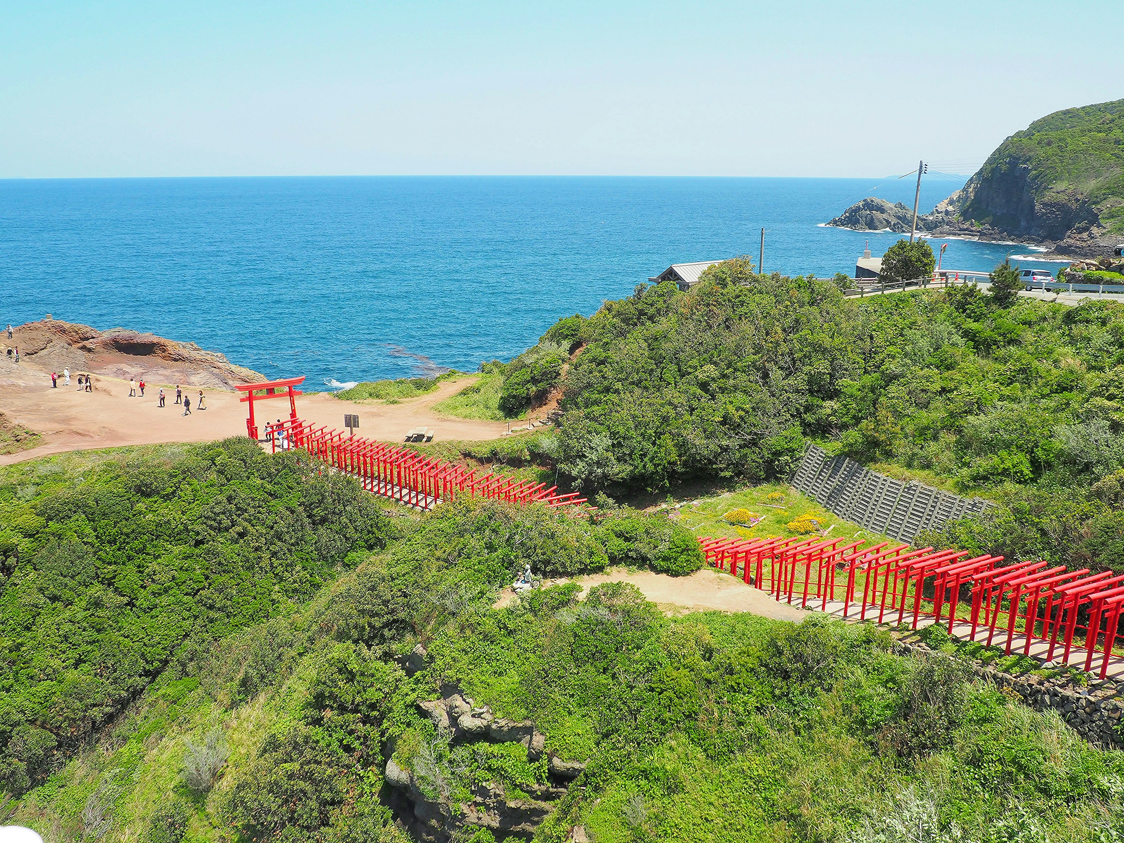 Path of red torii gates surrounded by green hills and blue sea