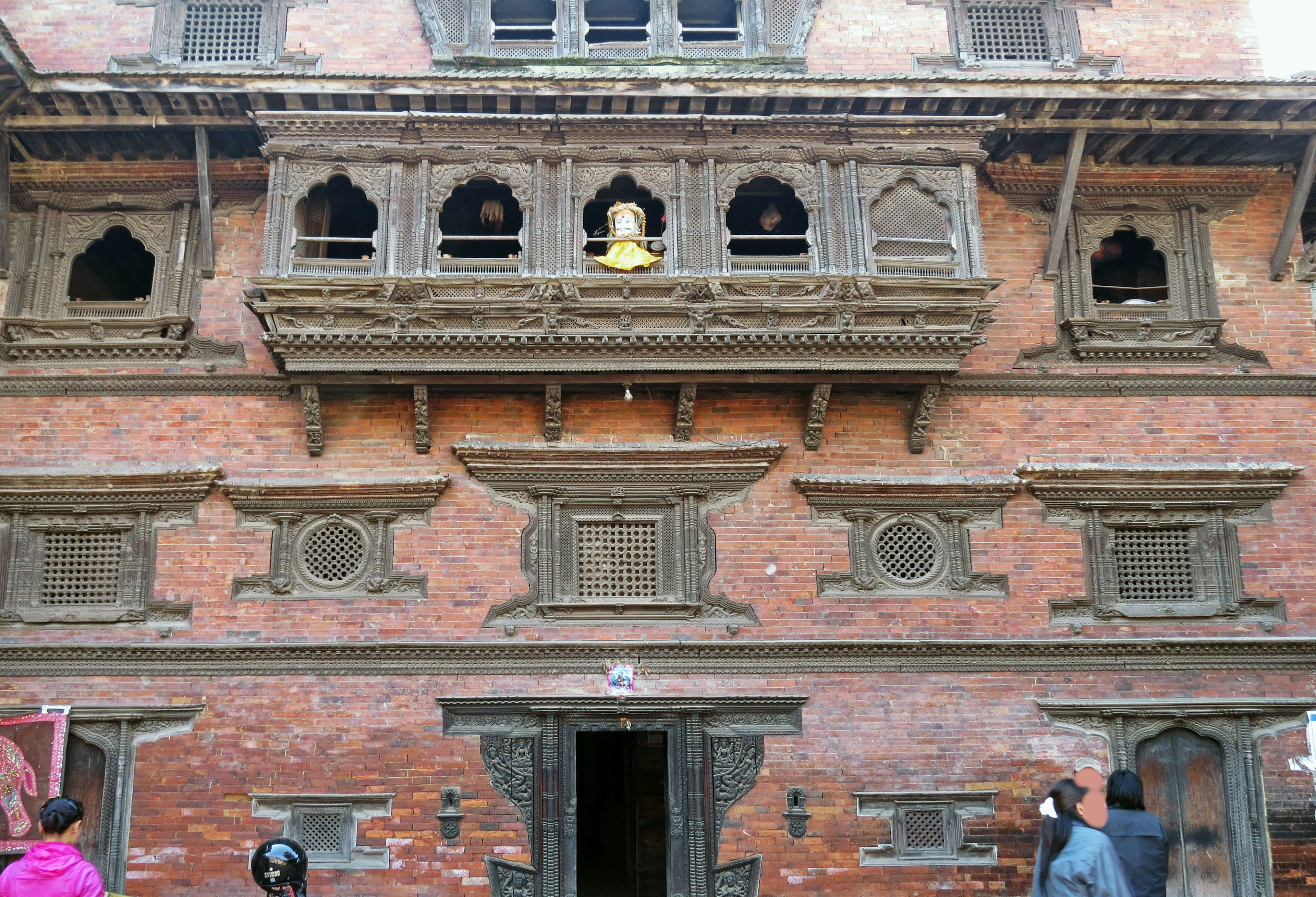 Bâtiment traditionnel en briques rouges au Népal avec des fenêtres en bois sculptées et une statue de Bouddha