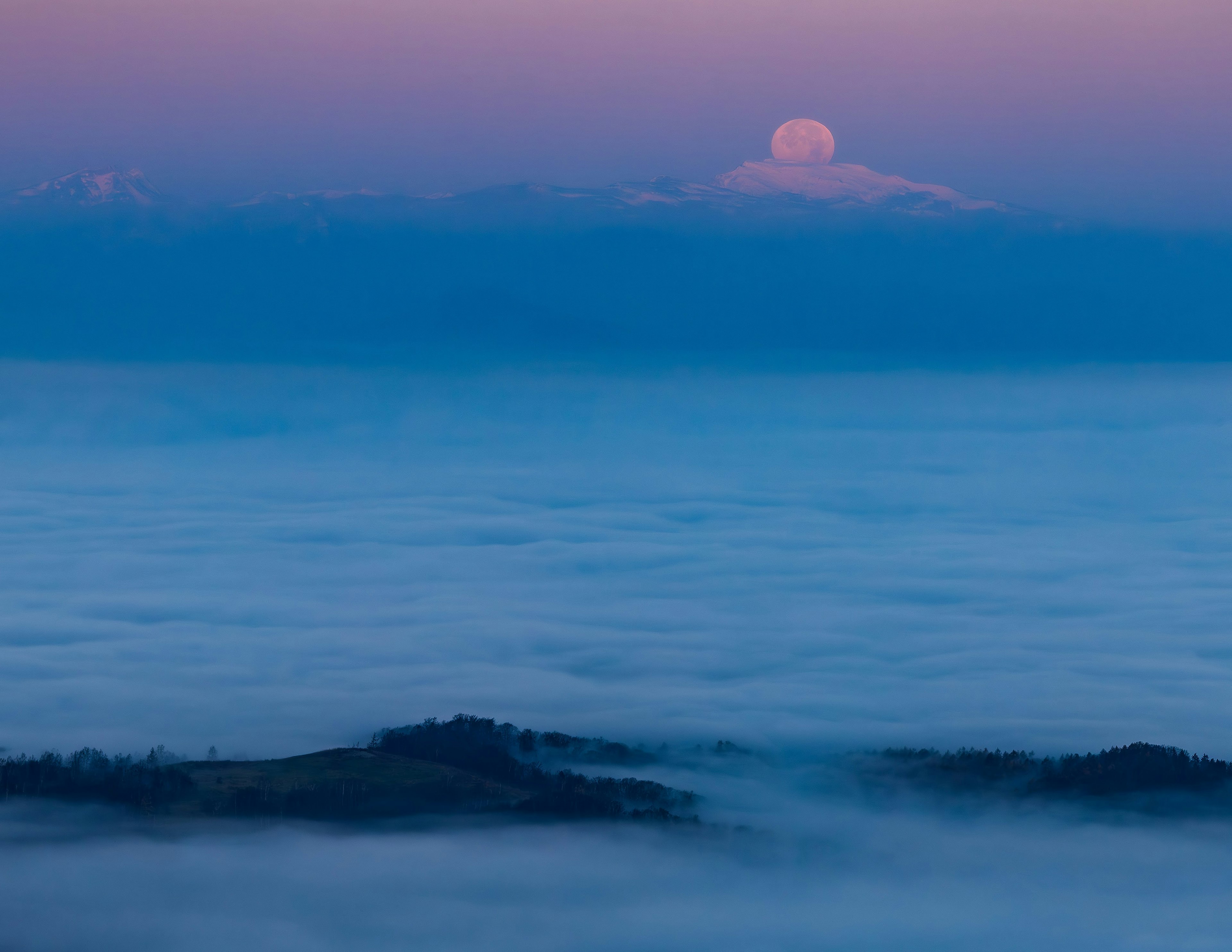 Silhouette of mountains in blue mist with the moon rising