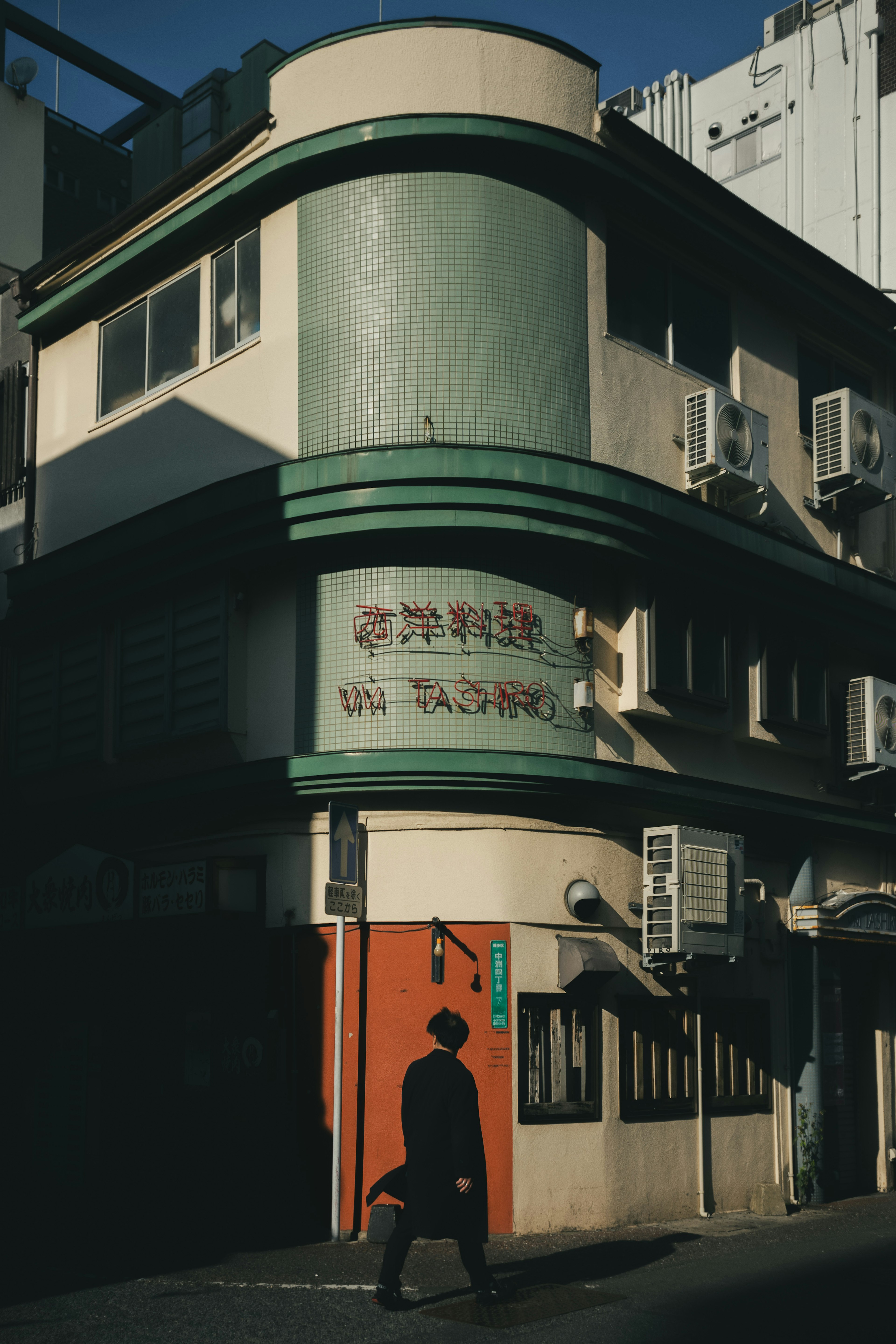 Un vieux bâtiment avec des accents verts et une personne marchant dans la rue