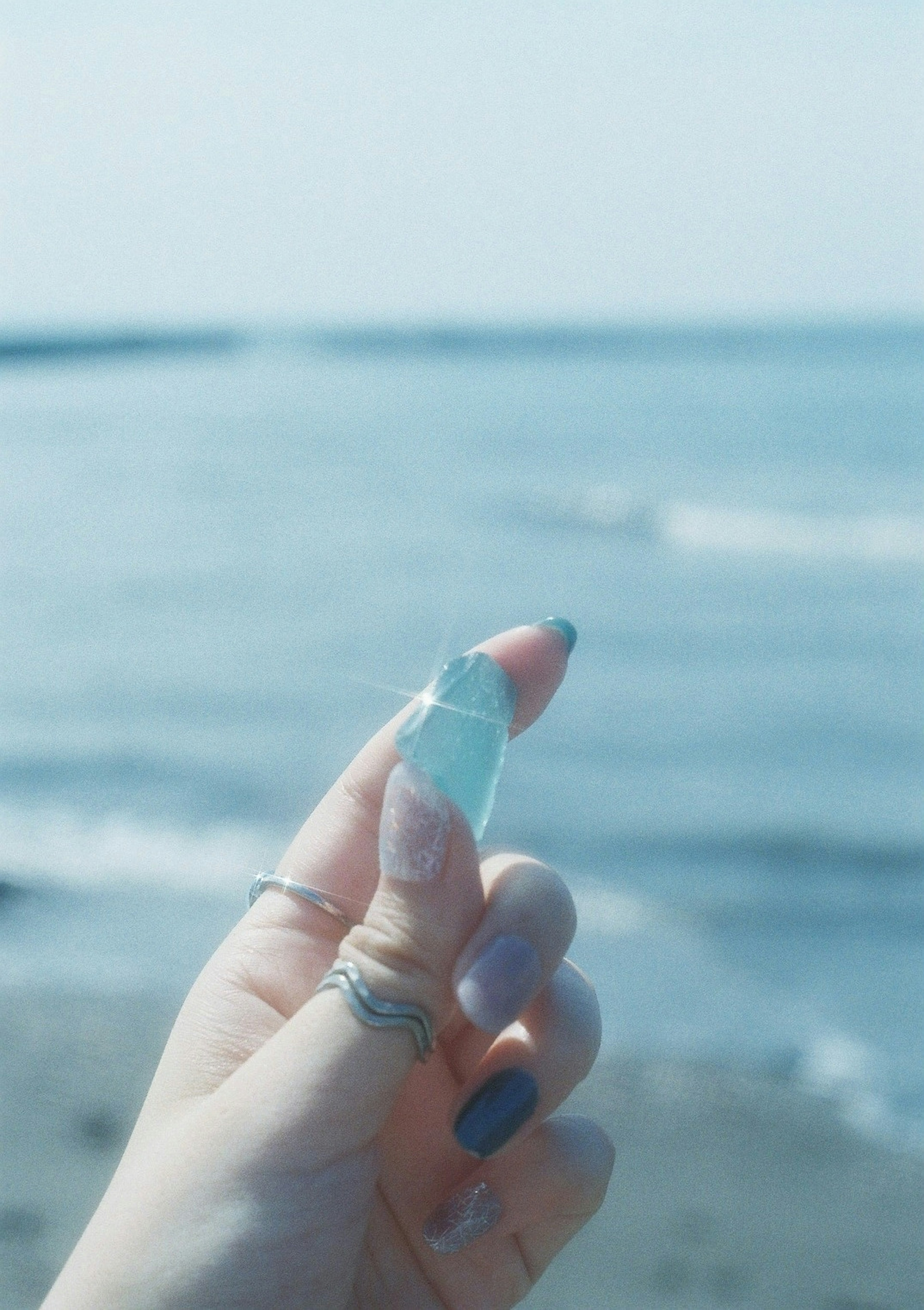 Hand holding a turquoise glass shard against a blue ocean