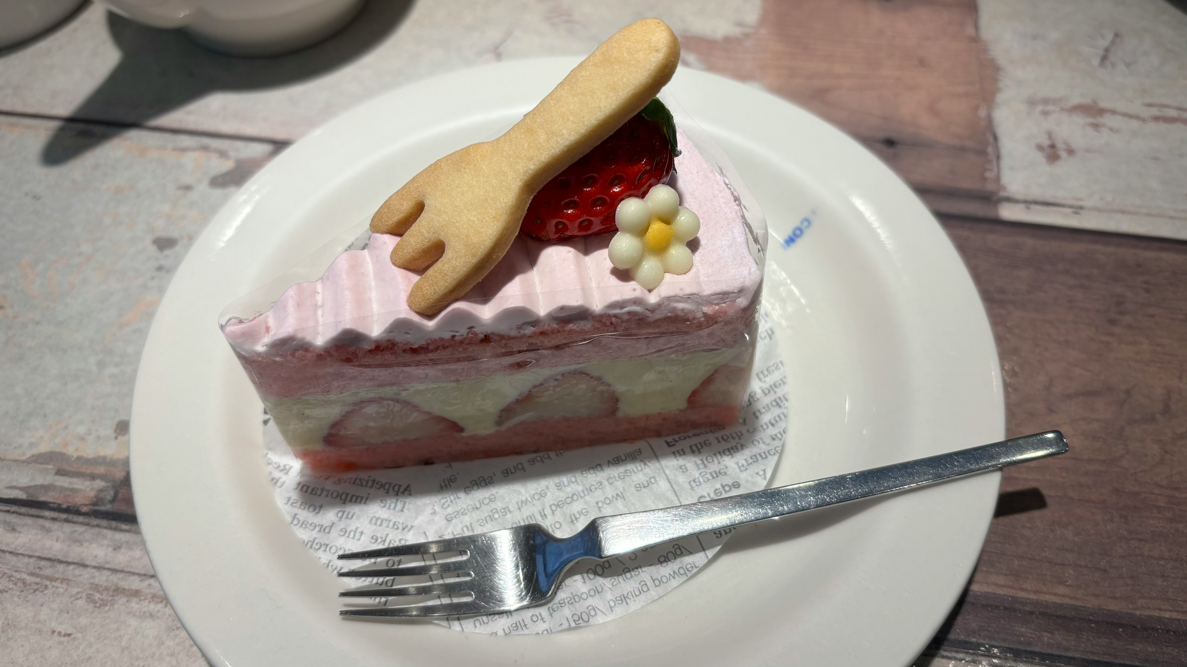 Slice of cake with pink cream and strawberry topping served on a white plate with a fork