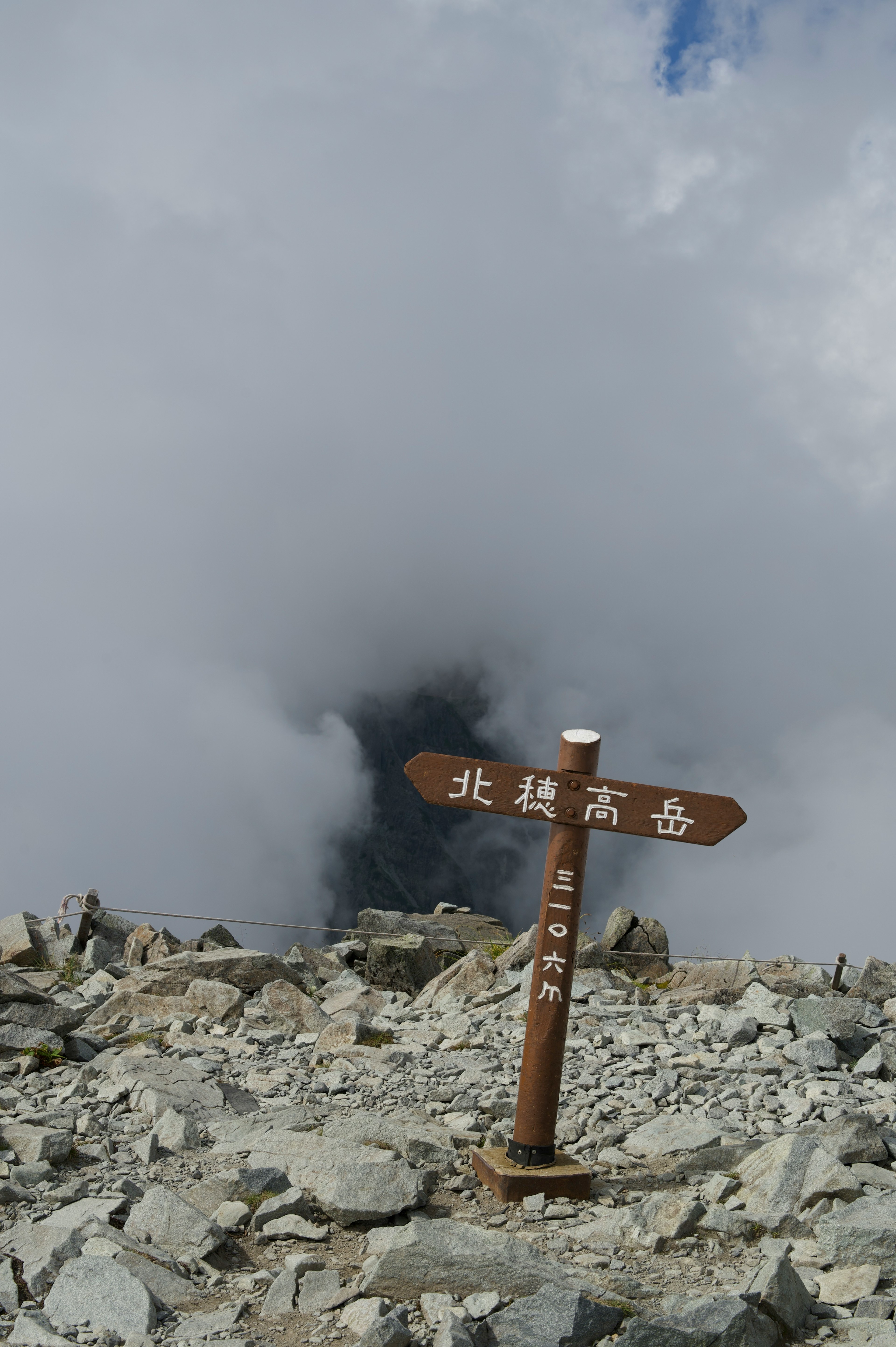 雲に囲まれた山頂の標識と岩場の風景