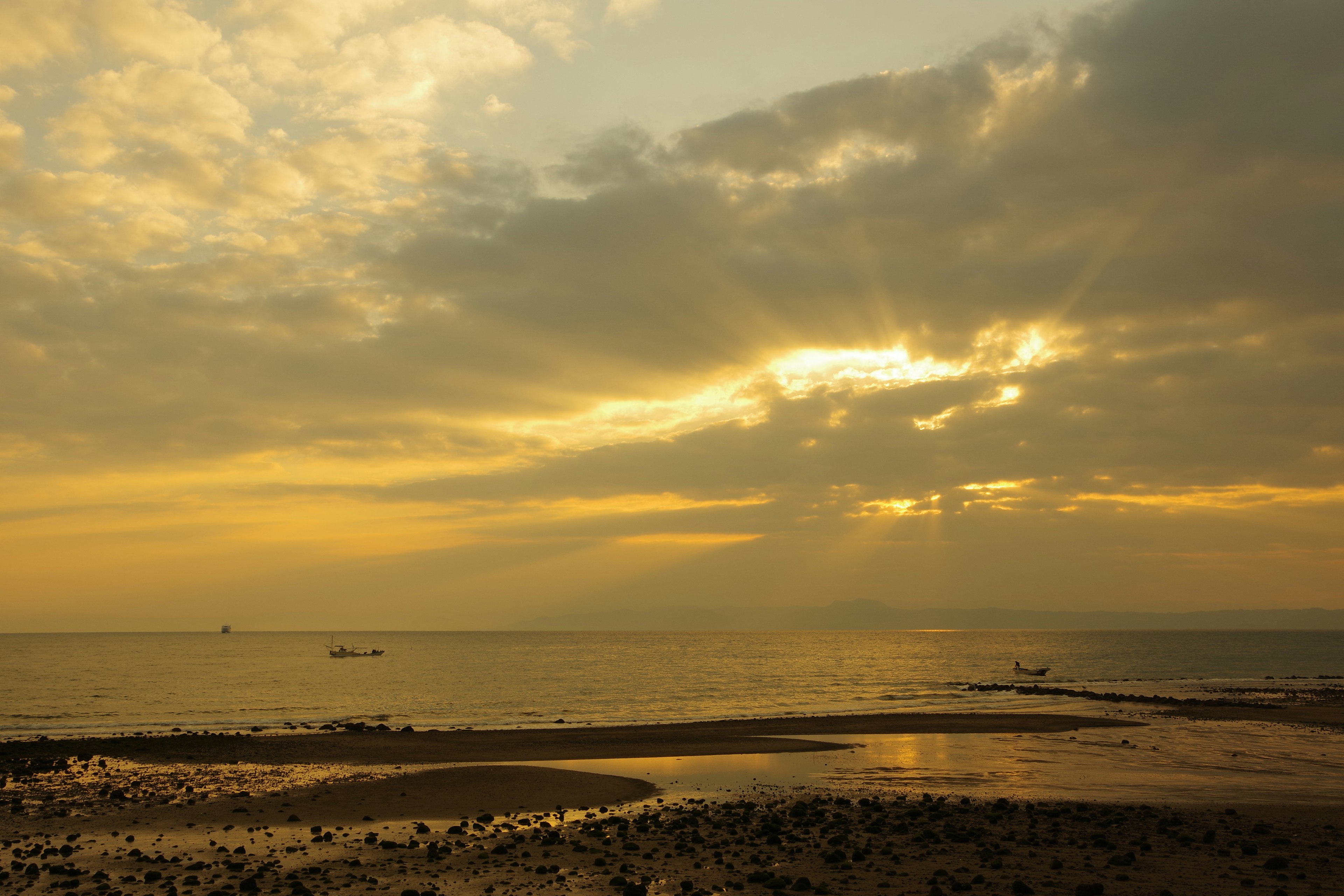 Sonnenuntergang über dem Meer mit orangefarbenem Himmel und Wolken, entfernte Boote sichtbar