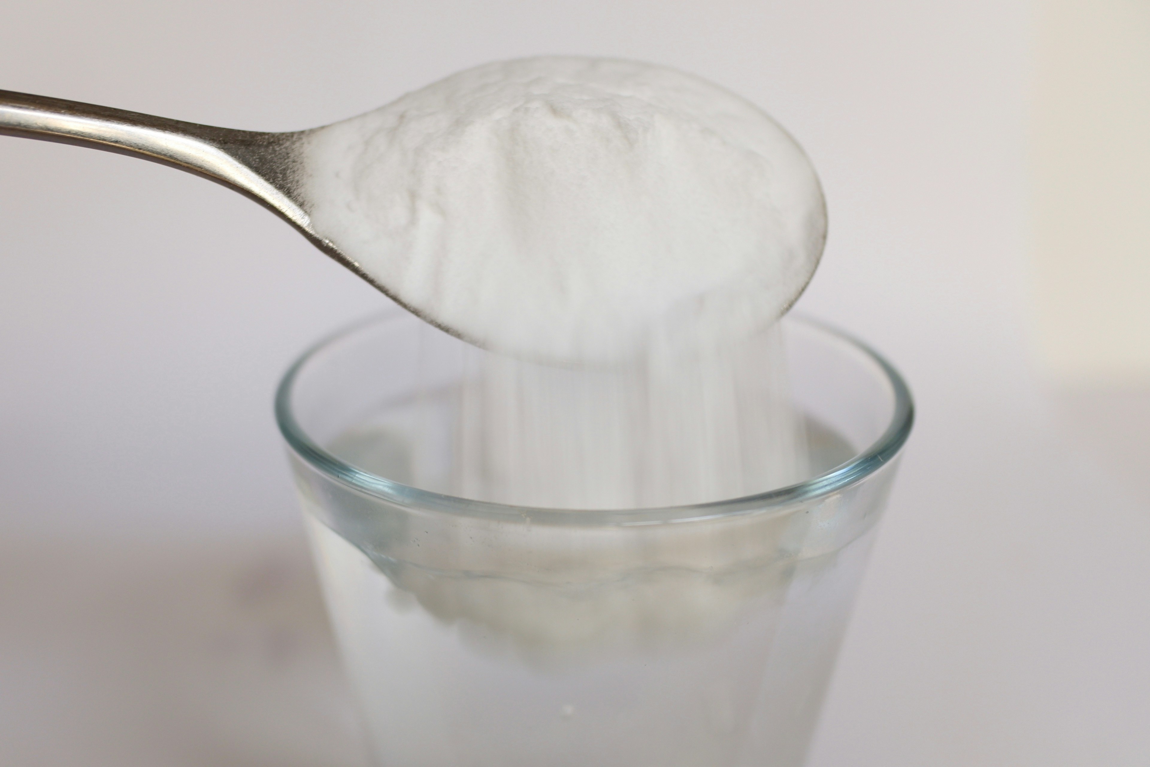 Cuillère versant de la poudre blanche dans un verre d'eau clair