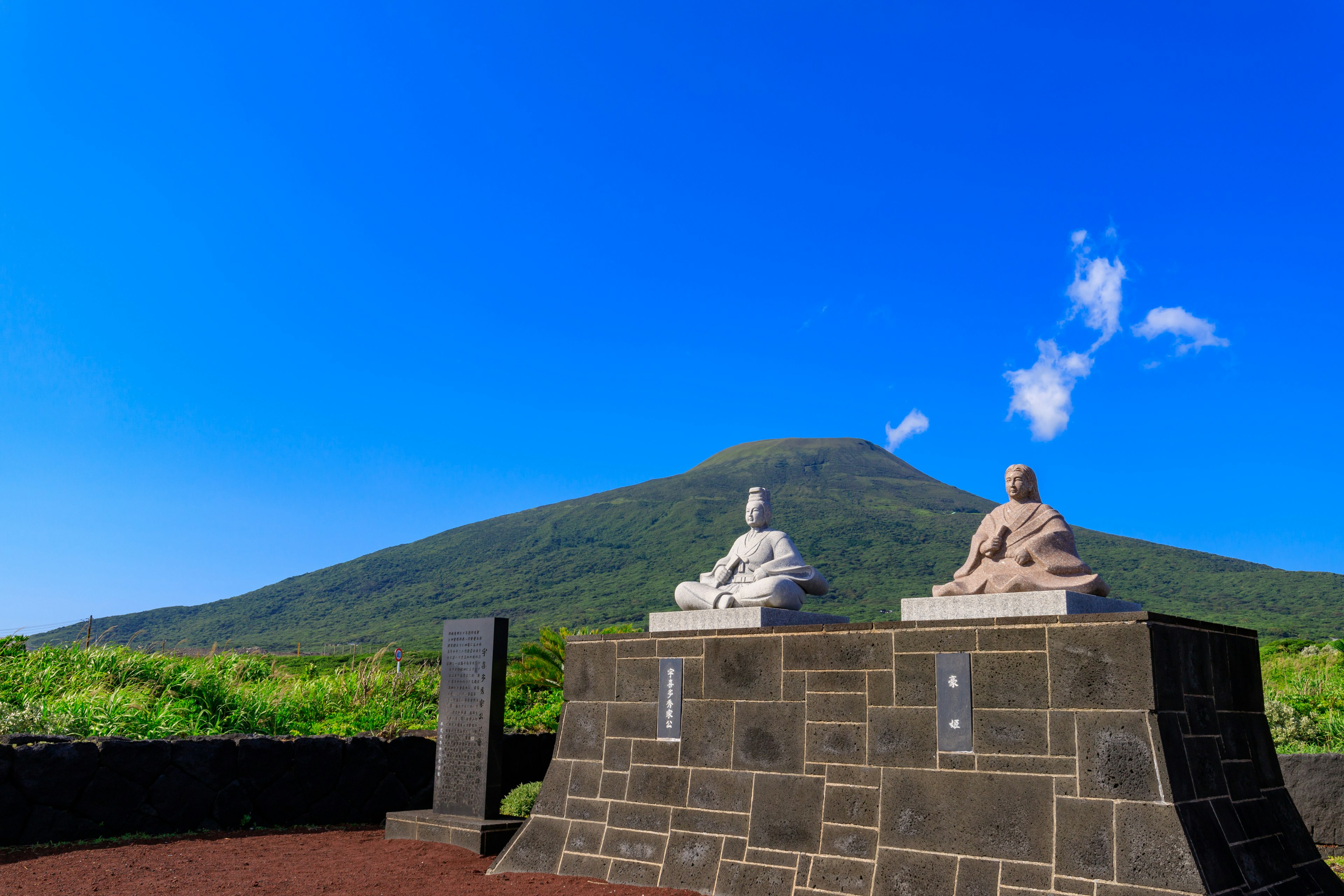 Two stone Buddha statues under a clear blue sky with a mountain in the background