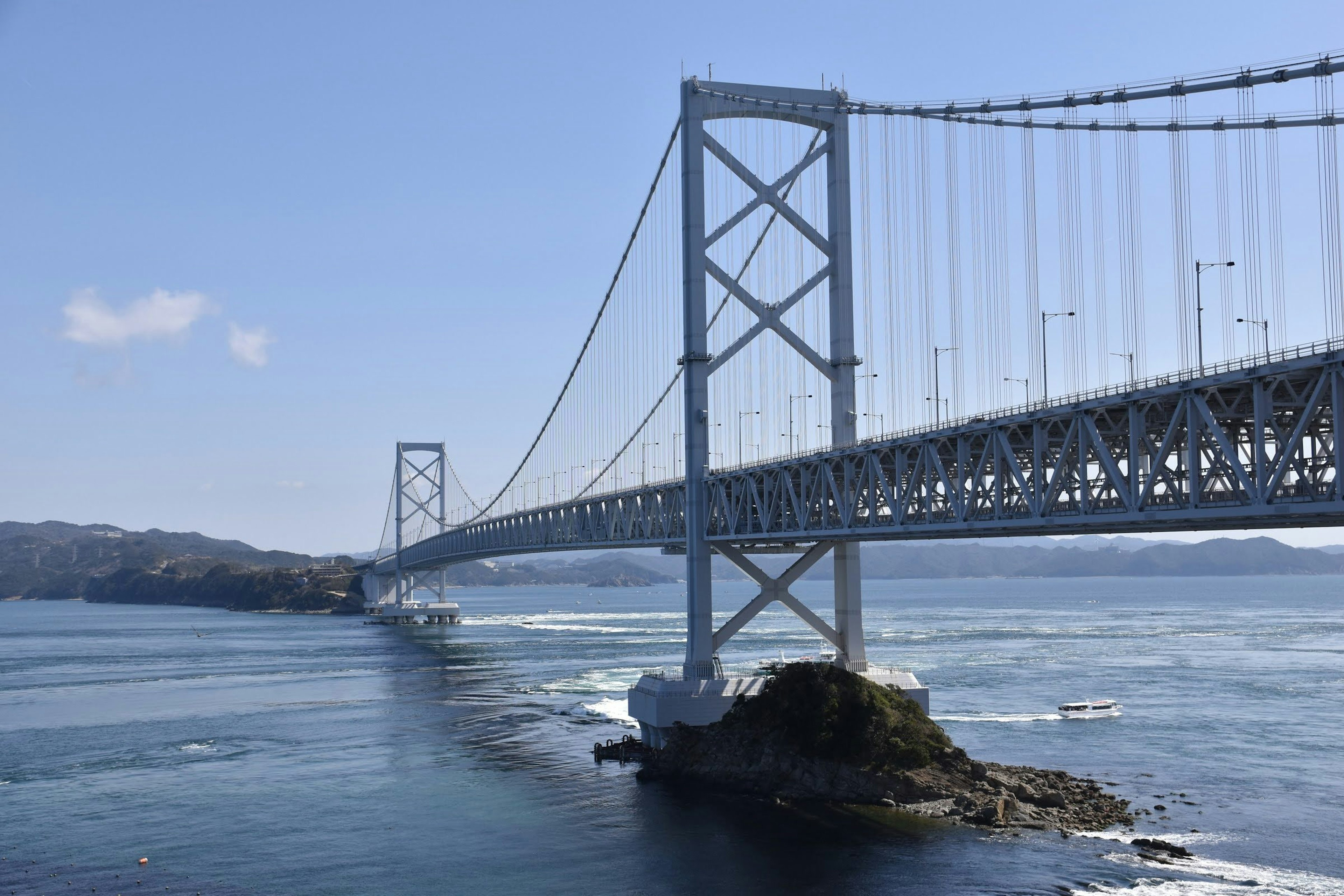 Jembatan Akashi Kaikyō melintasi laut dengan langit biru dan ombak yang terlihat