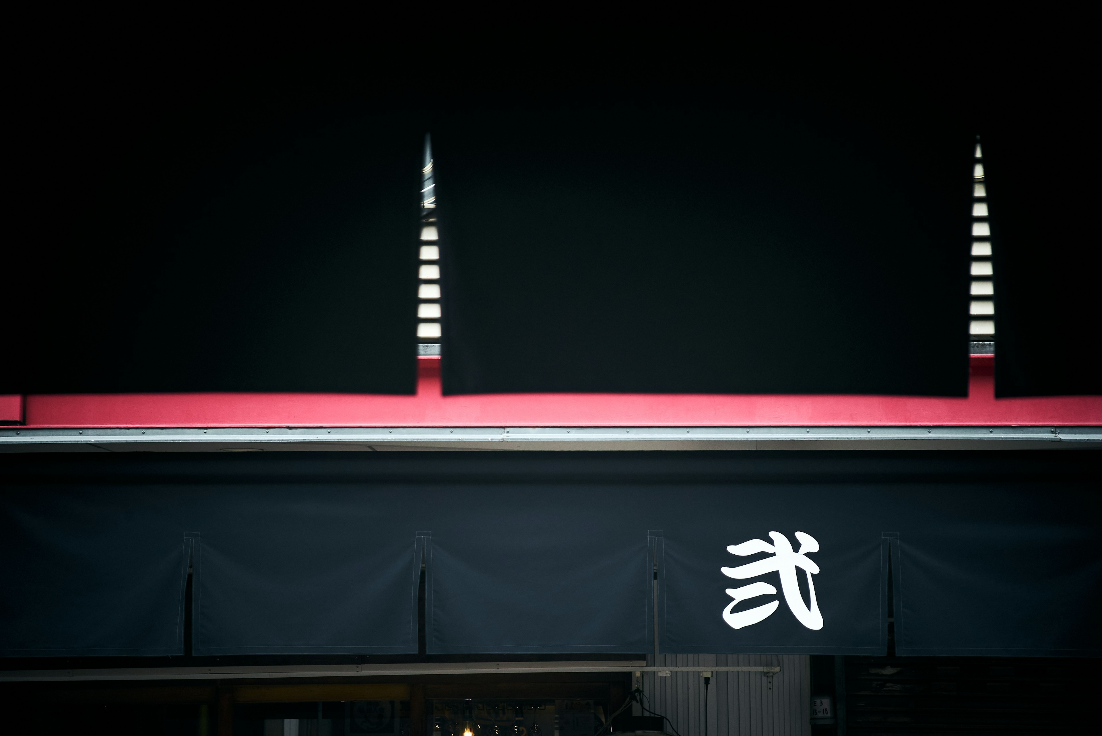 A storefront with a black facade featuring a red stripe and a white kanji sign in the center