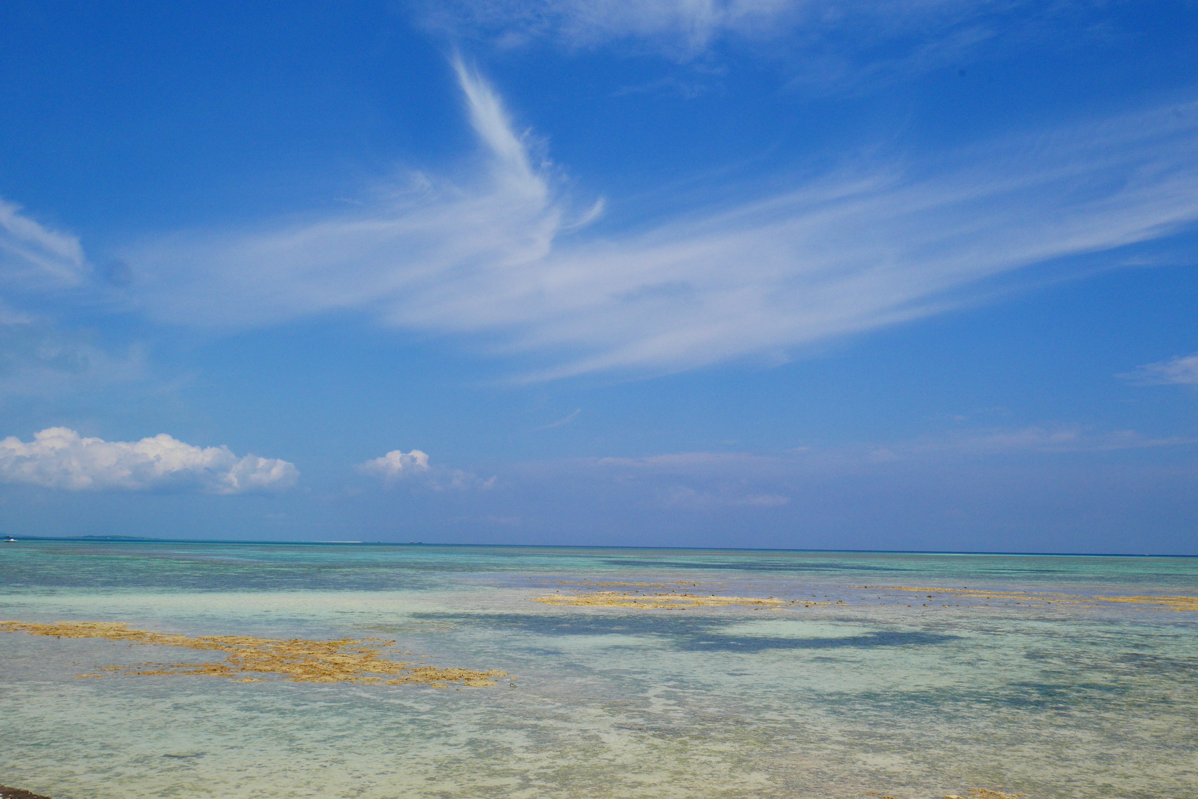 Blue sky over a clear ocean with scattered clouds