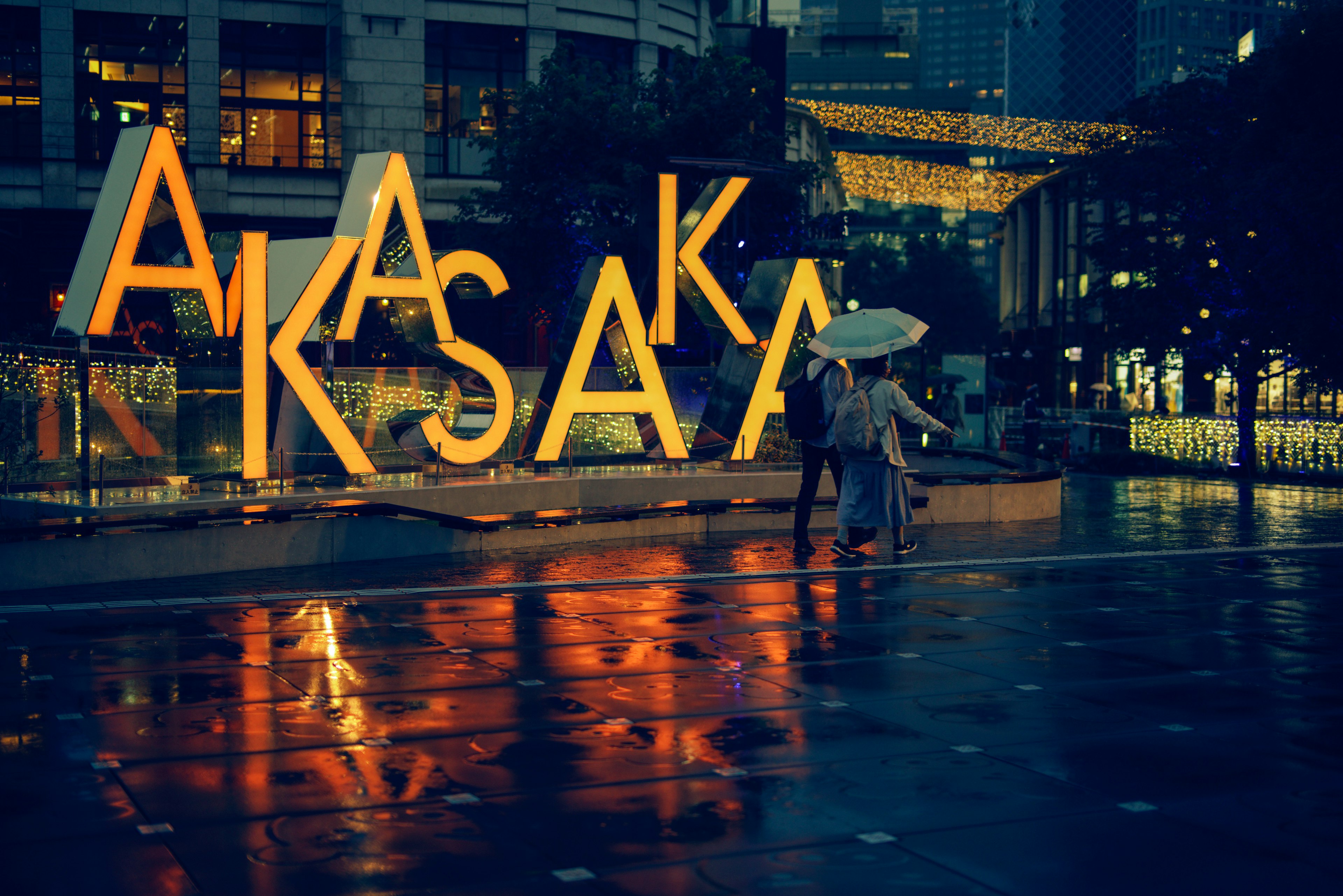 Large illuminated sign of Akasaka with people holding umbrellas in the rain