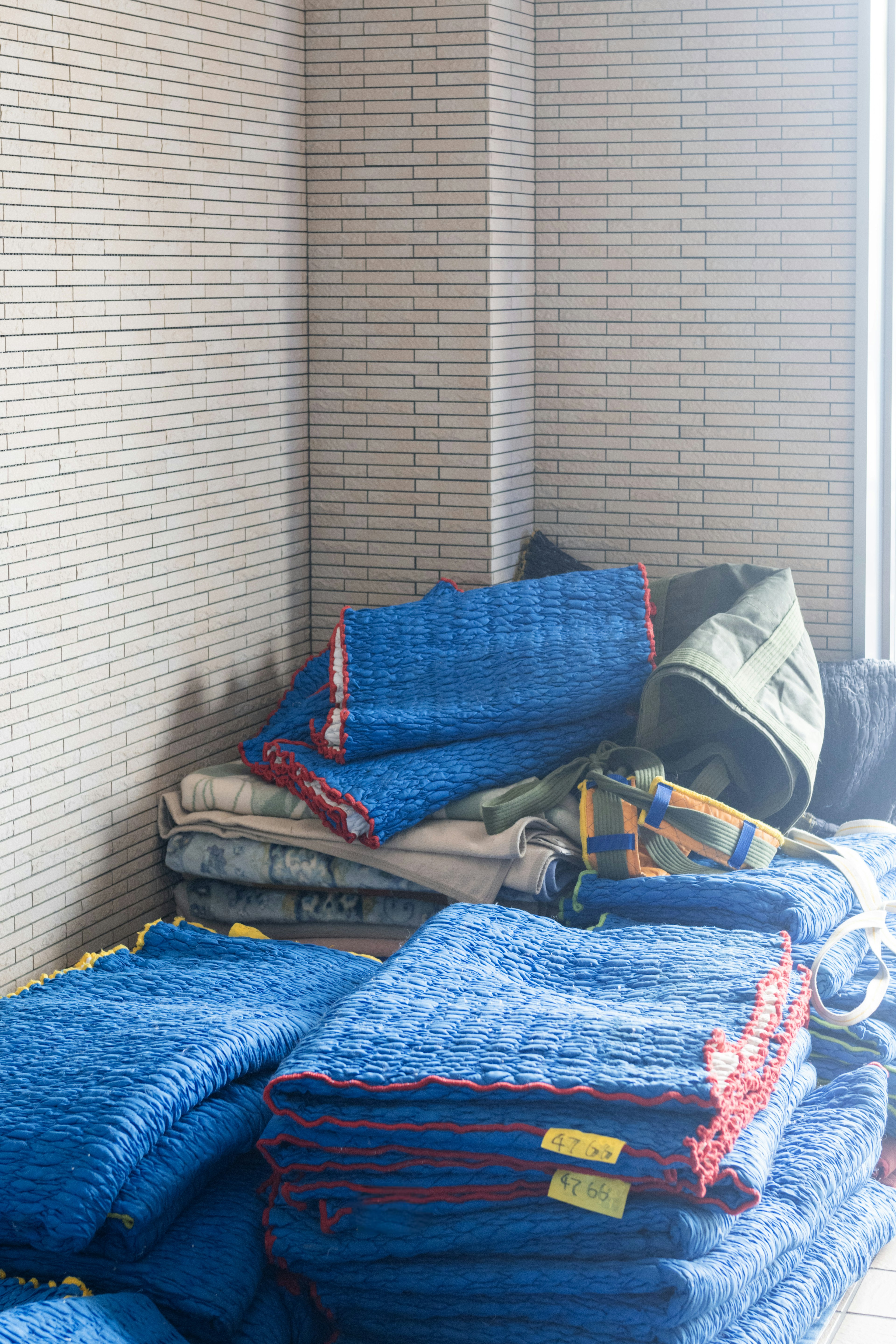 A corner of a room with stacked blue blankets and a green bag